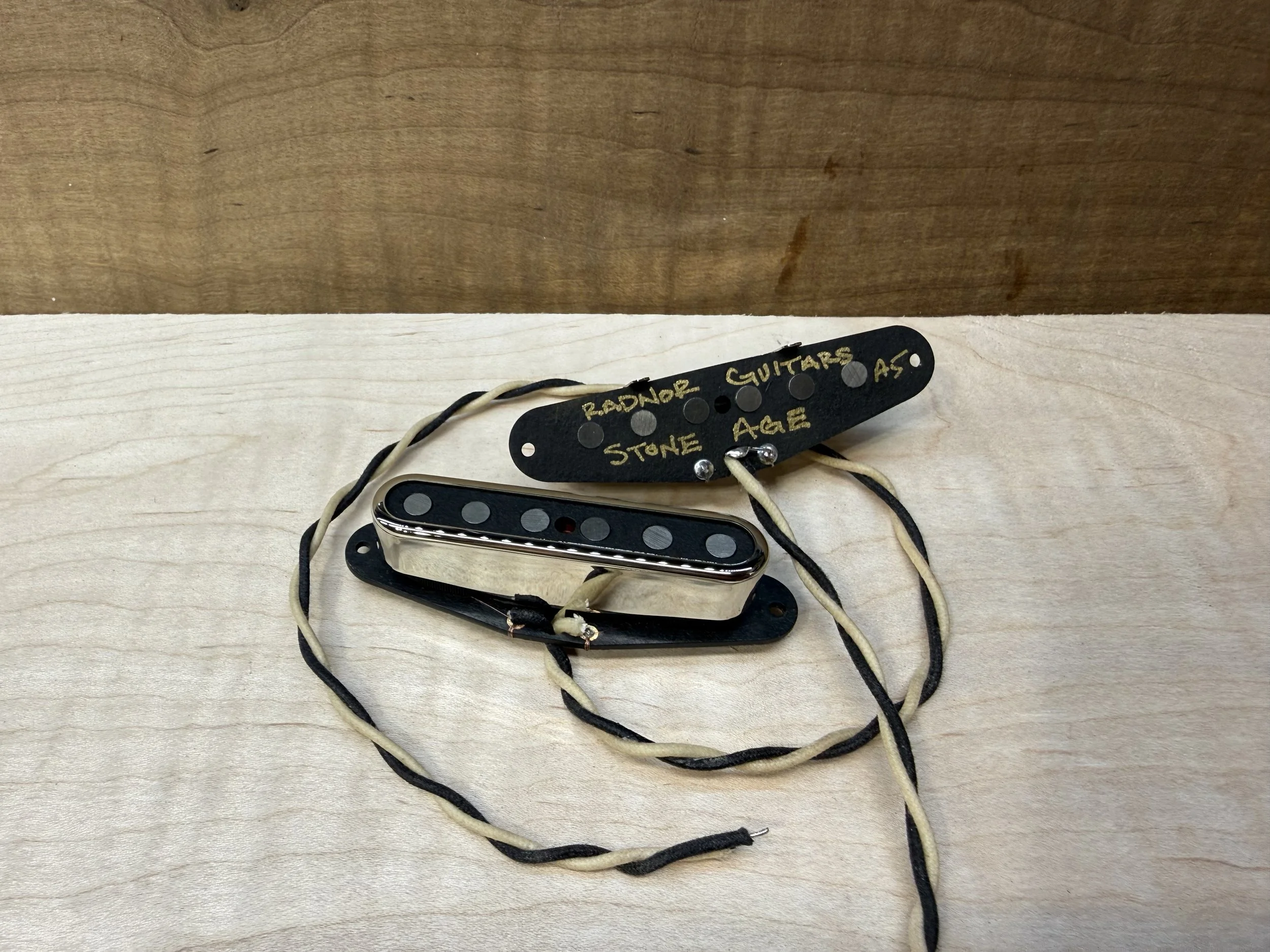 A single coil telecaster guitar neck pickup with black and white wires and a black mounting plate labeled 'RADNDOR GUITARS' and 'STONE AGE' on a wooden surface. radnor guitars stone age neck pickups