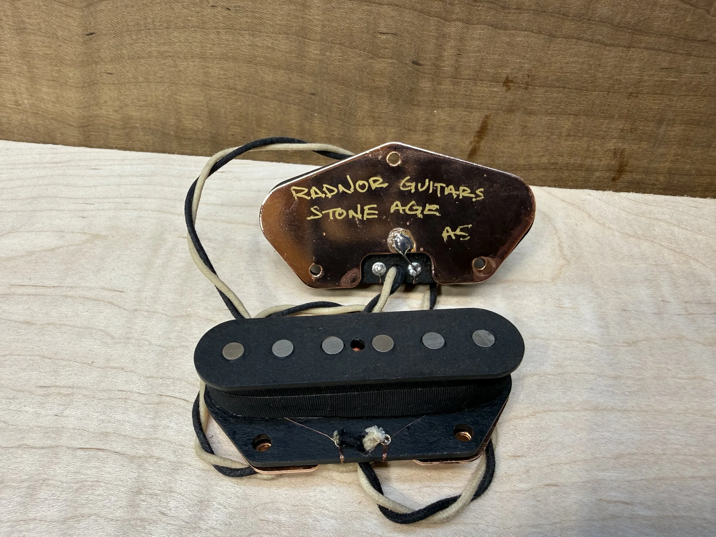 Close-up image of a telecaster single coil bridge pickup attached to a wooden surface, with black and white wires and copper plated base plate. radnor guitars stone age telecaster bridge pickups.