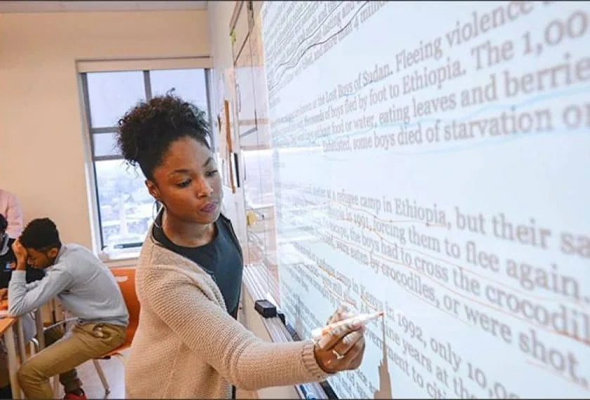 Woman writing on an interactive whiteboard while students sit at desks in a classroom setting