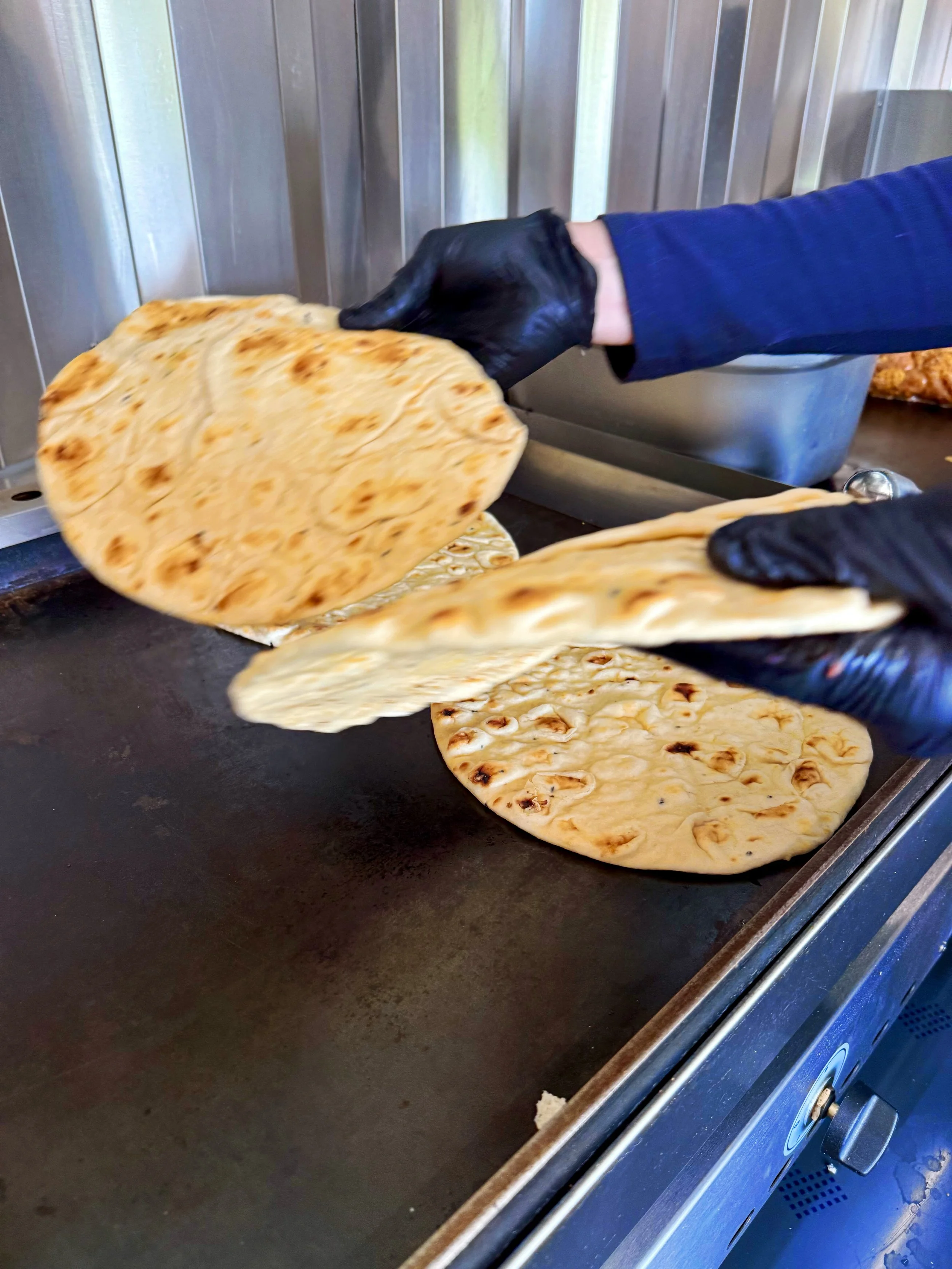 Person cooking or preparing naan bread on a griddle, flipping the bread with gloved hands.