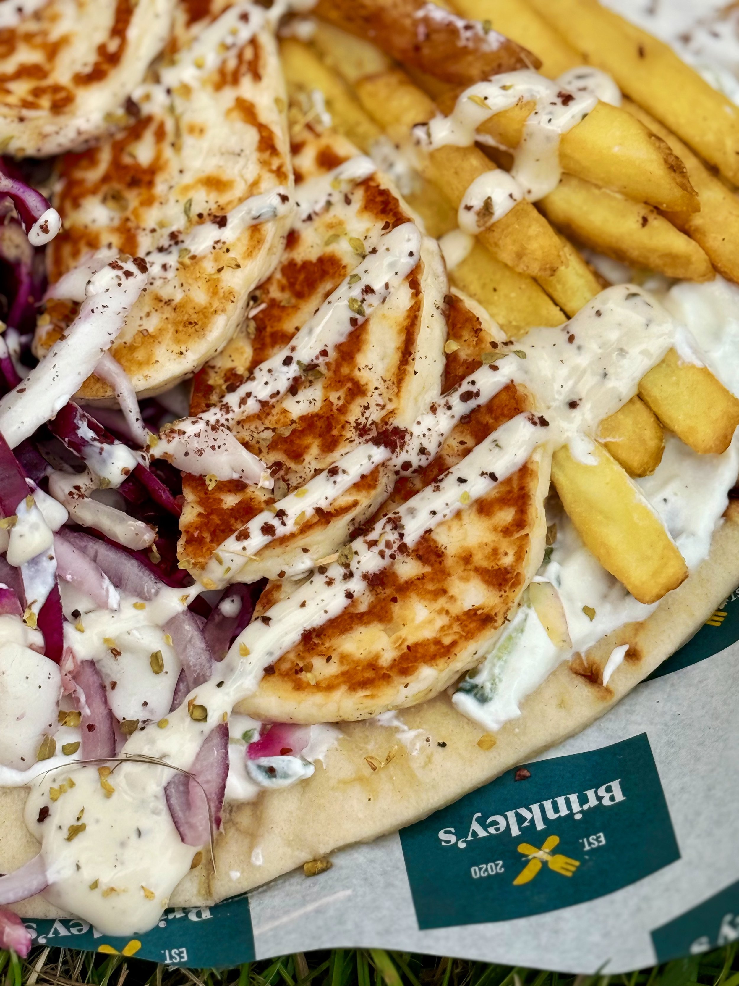 Grilled halloumi gyros with fries, red onion, and creamy dressing on a flatbread wrap