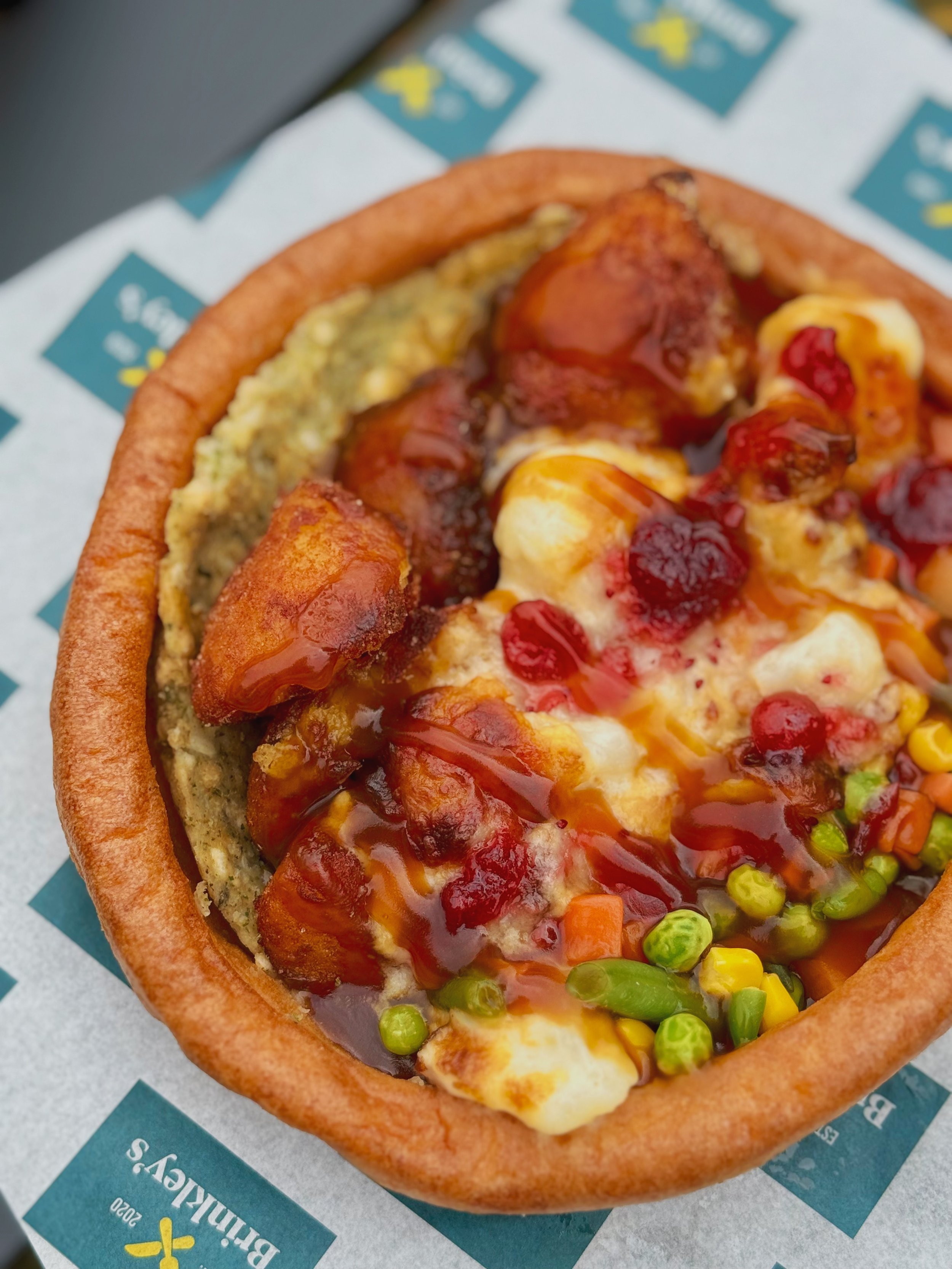 Close-up of a stuffed yorkshire pudding with stuffing, roast potatoes, cauliflower cheese, cranberry saurce and vegetables drizzled with grazy.