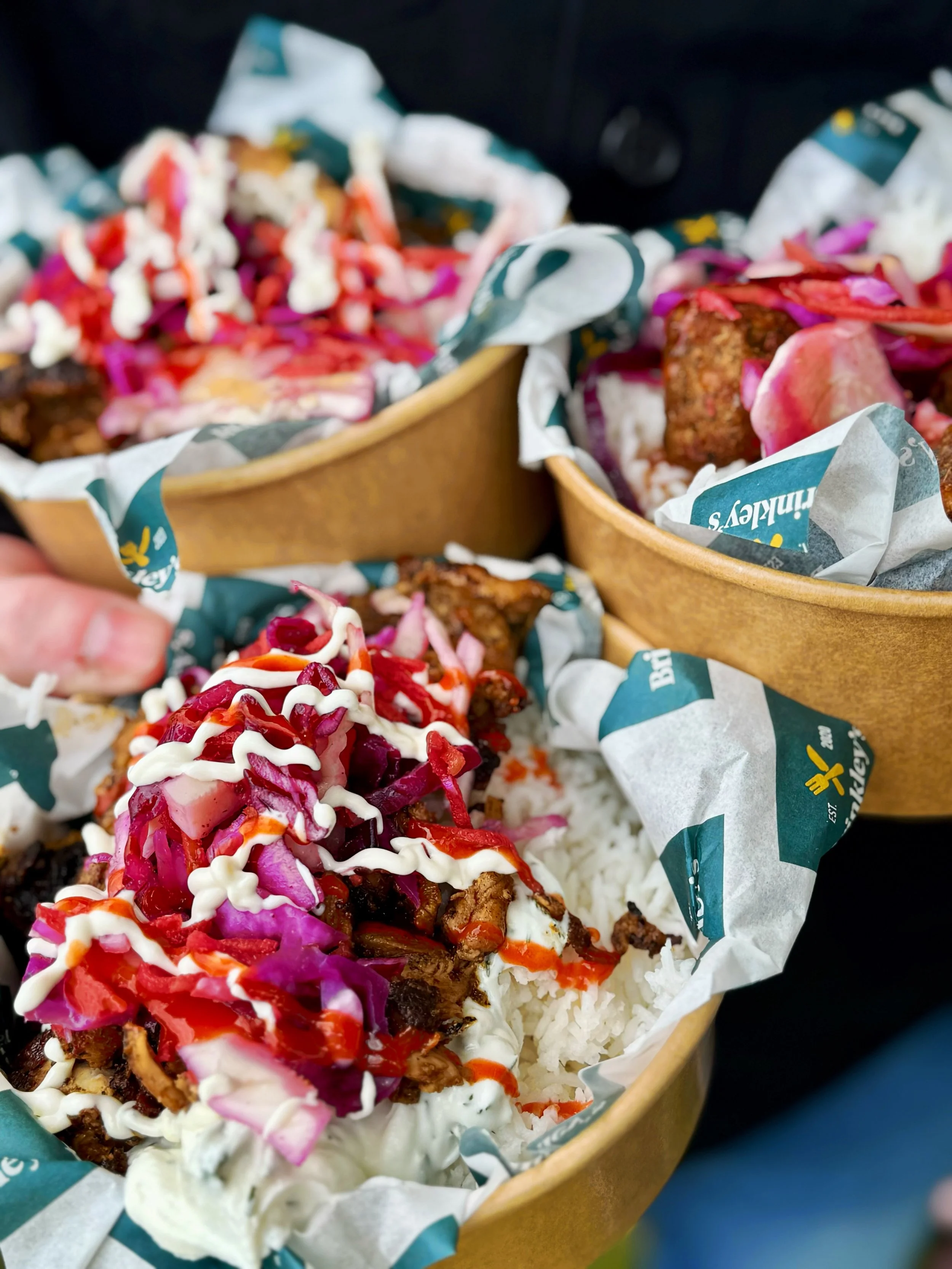 Three bowls of Mexican street food, likely tacos or similar dishes, topped with colorful shredded vegetables, sauces, and garnishes, with corn and rice visible on the plates.