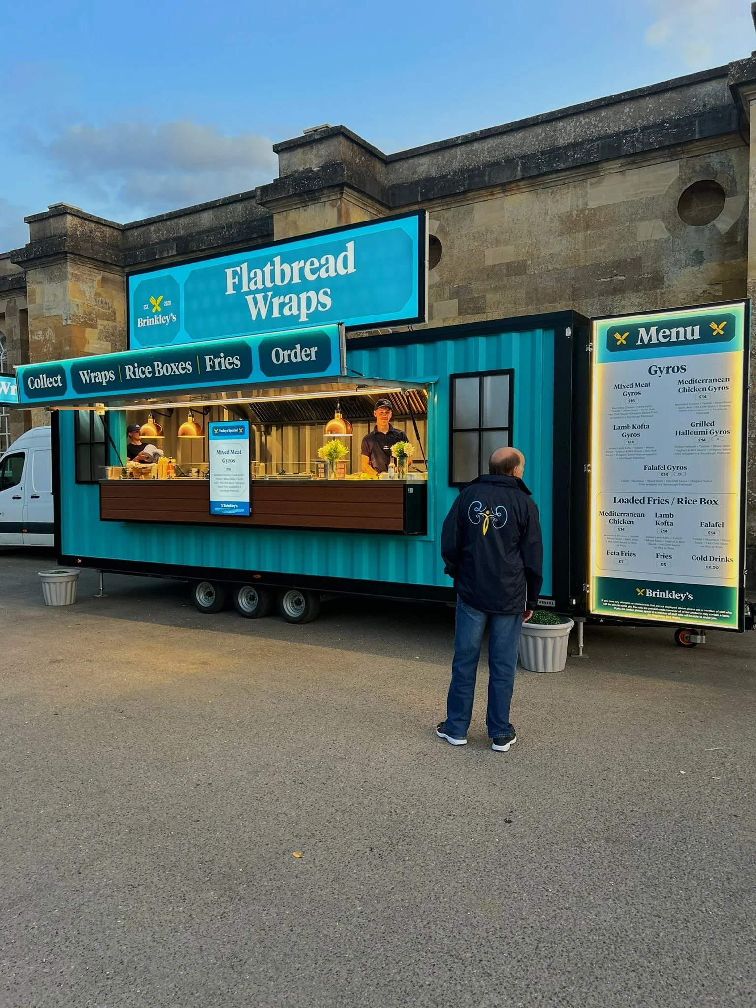 Food truck named 'Flatbread Wraps' serving gyros and other Mediterranean dishes, with a customer standing in front of it.