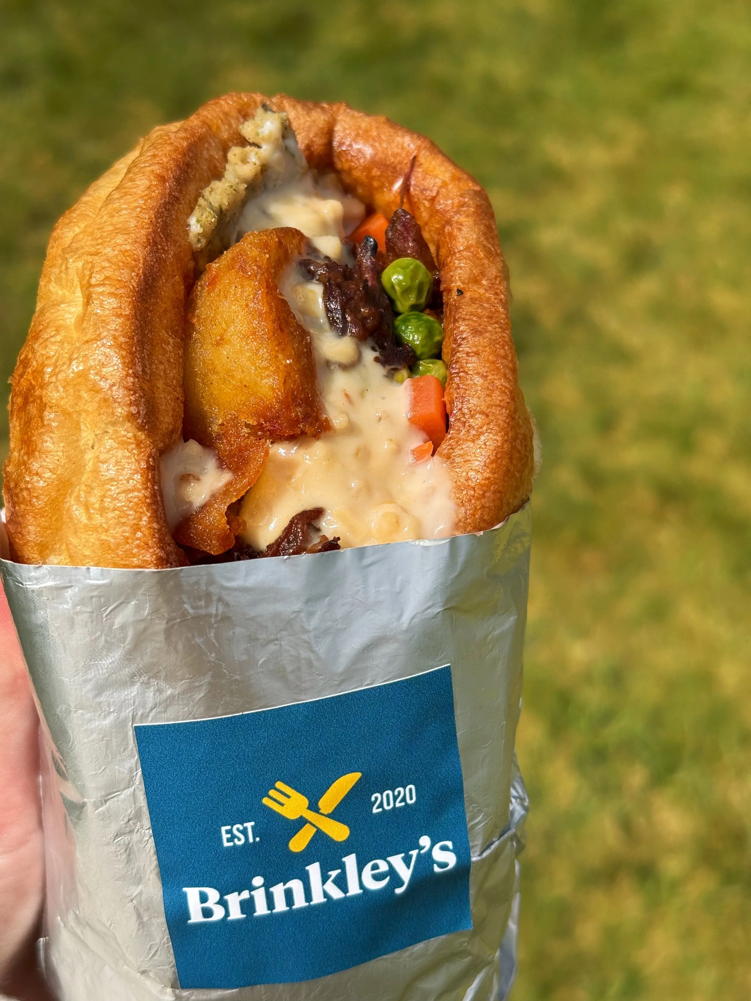 Close-up of a loaded fish sandwich with fried fish fillet, tartar sauce, and vegetables in a foil wrapper with a Brinkley's logo.