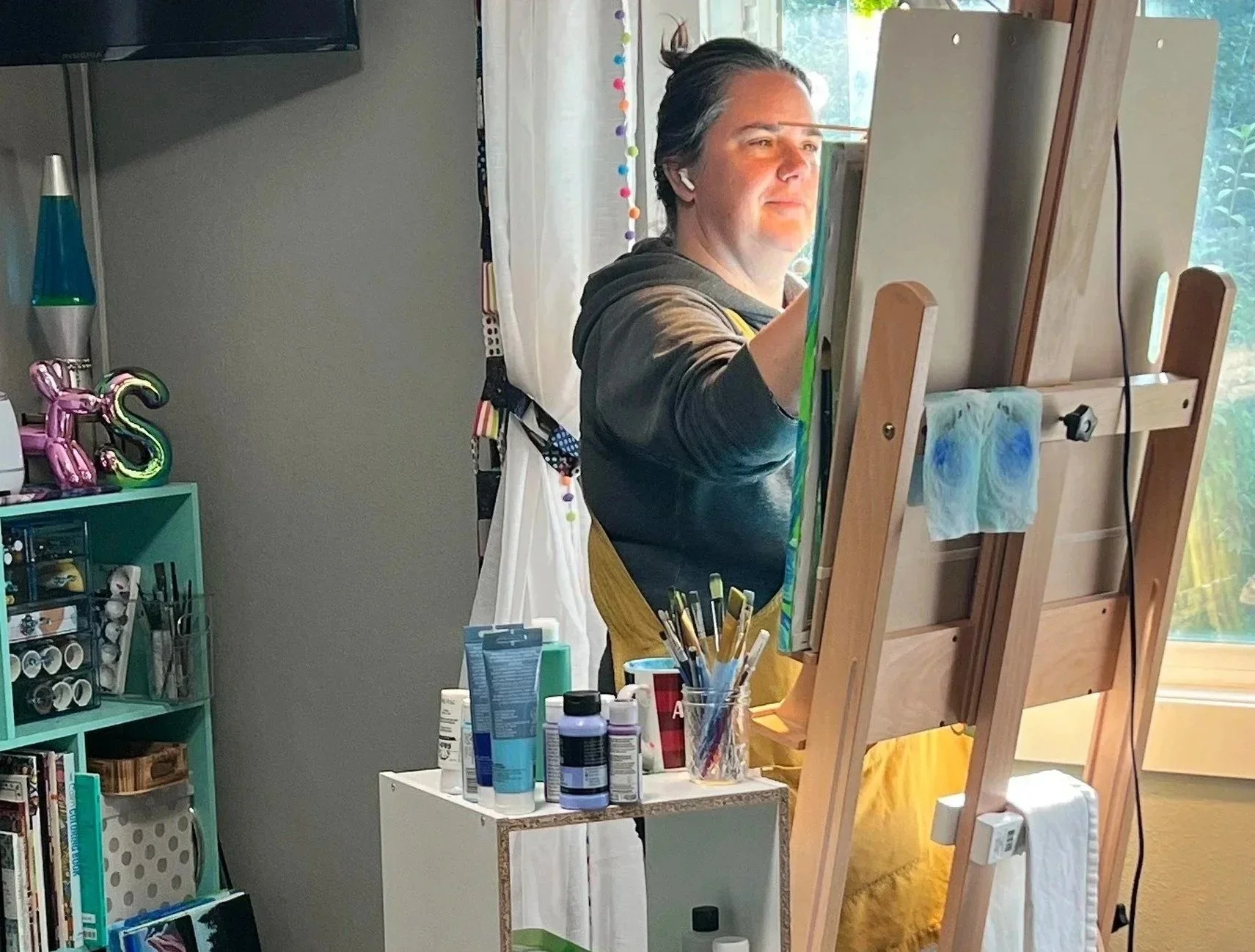 Sara Allen painting on a canvas easel in a room with art supplies and natural light from a window.