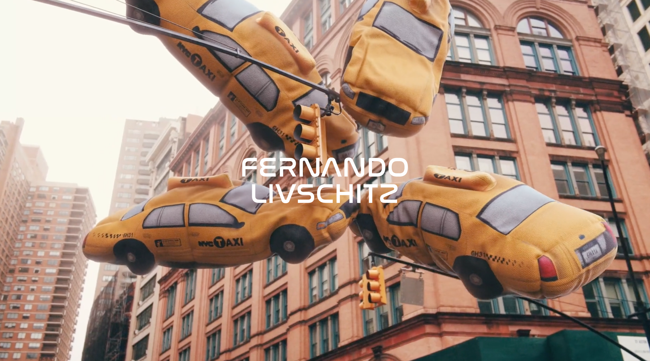 Yellow fabric taxis hanging as decorations in an urban city street, with tall buildings and traffic lights in the background.