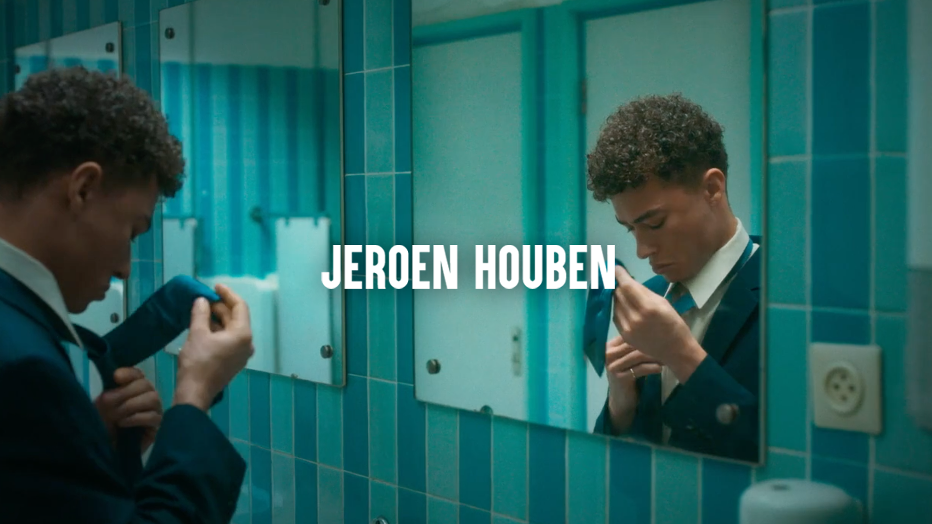 A young man in a school uniform stands in front of a mirror in a bathroom with teal tiles. He is adjusting his tie, looking down with a focused expression. The reflection in the mirror shows him holding his tie close to his chest. The name "Jeroen Houben" is displayed in bold white text across the center of the image.