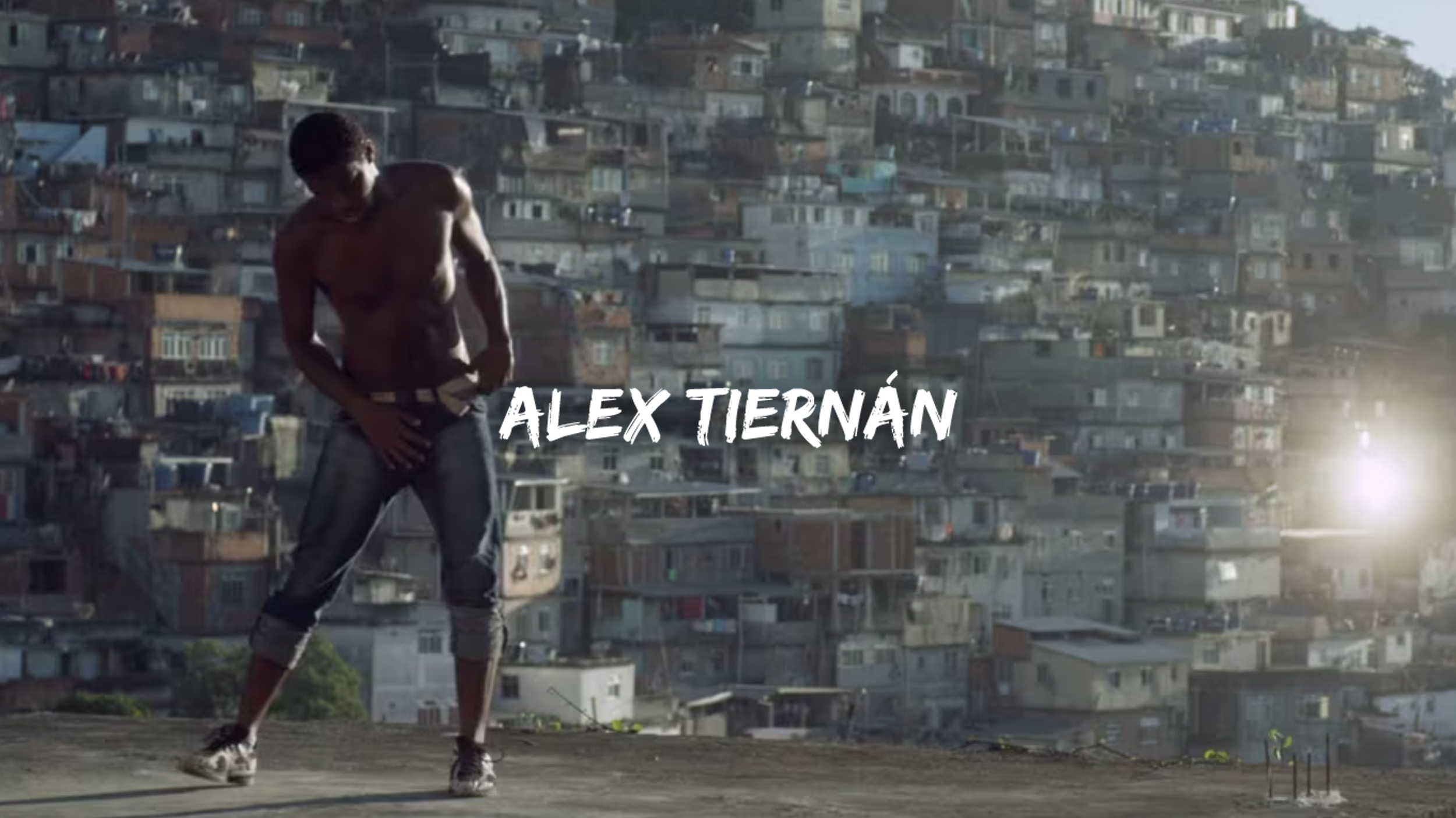 A shirtless young man with curly hair dancing on a rooftop with a densely populated urban area in the background; the name 'ALEX TIERNÁN' is displayed across the image.