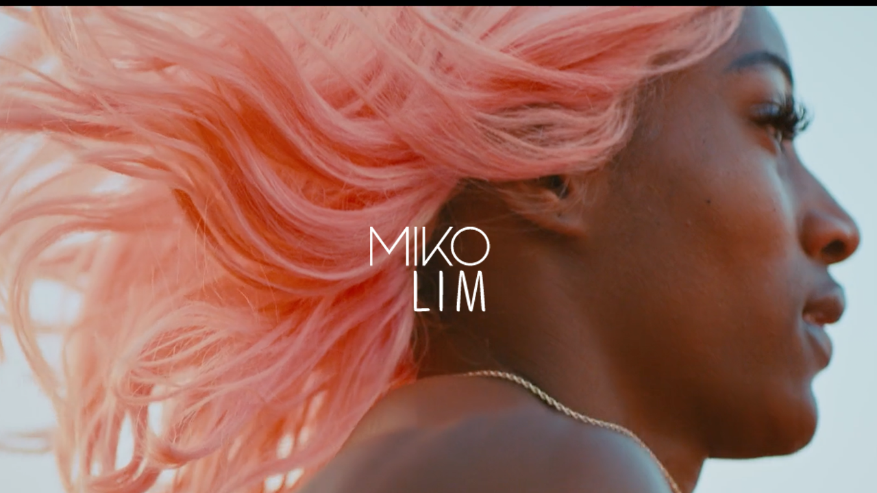 Close-up of a woman with pink, wavy hair and dark skin, facing right, with the text 'MIKO LIM' overlayed in the center.