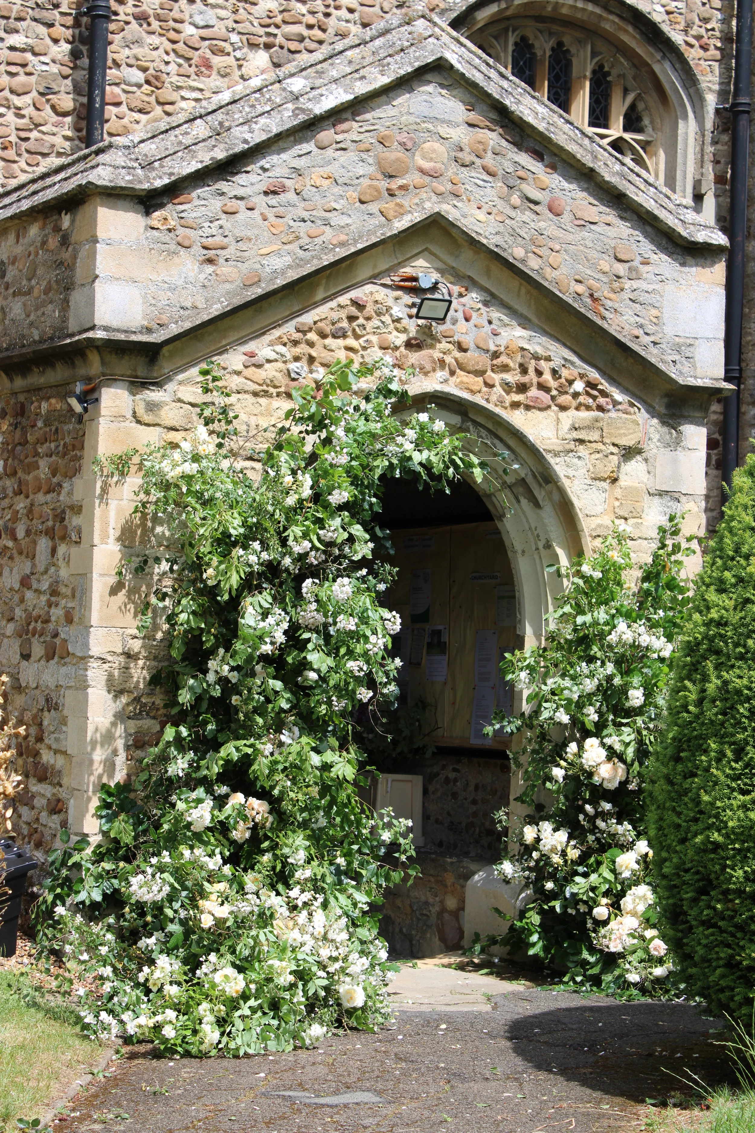 Stone church entrance framed by blooming white flowers and green shrubs.