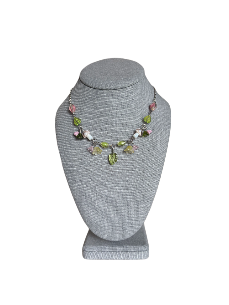 Green glass leaf charm necklace with pink accents and mushroom beads shown on a gray jewelry display