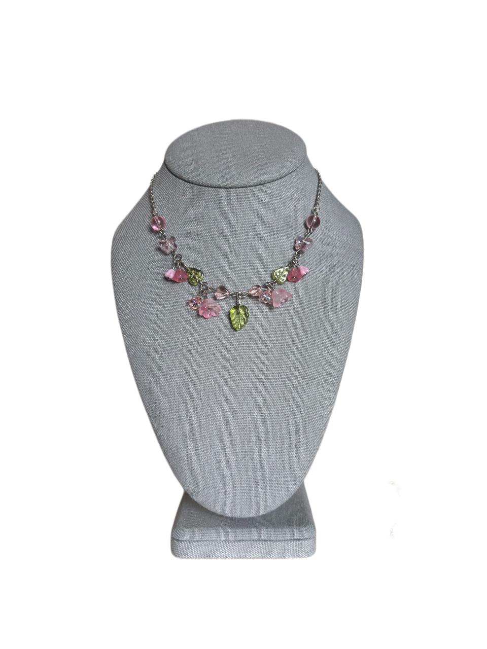 Pastel pink and green glass leaf charm necklace with hearts and flowers displayed on a gray stand