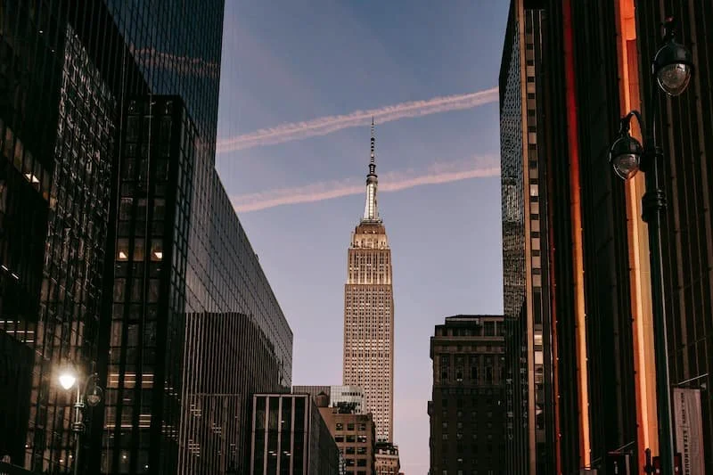 View of the Empire State Building in New York City during twilight, surrounded by modern office buildings.