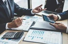 Business professionals discussing financial charts and data on a tablet and printed papers.