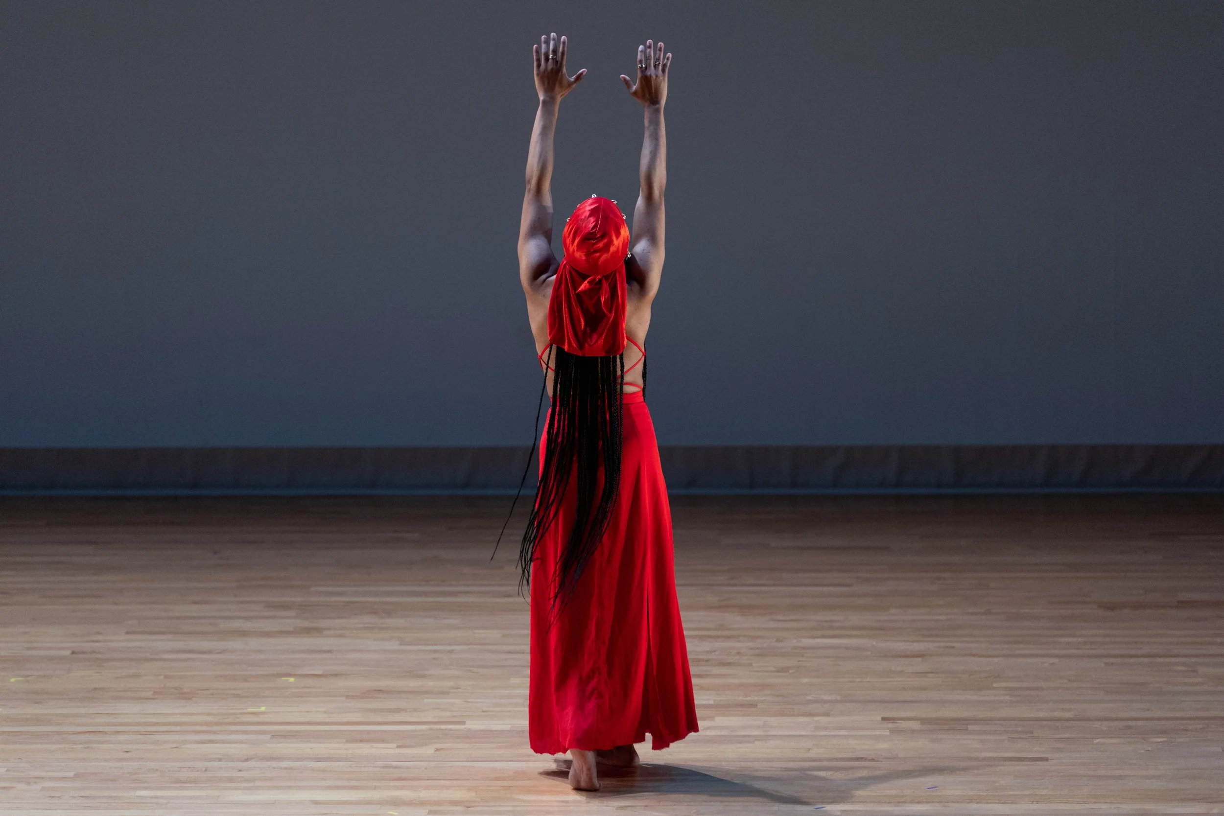 Aquilah Ohemeng professionally known as "KHILA"wearing a red dress and headscarf performing a dance on a stage with a dark background.
