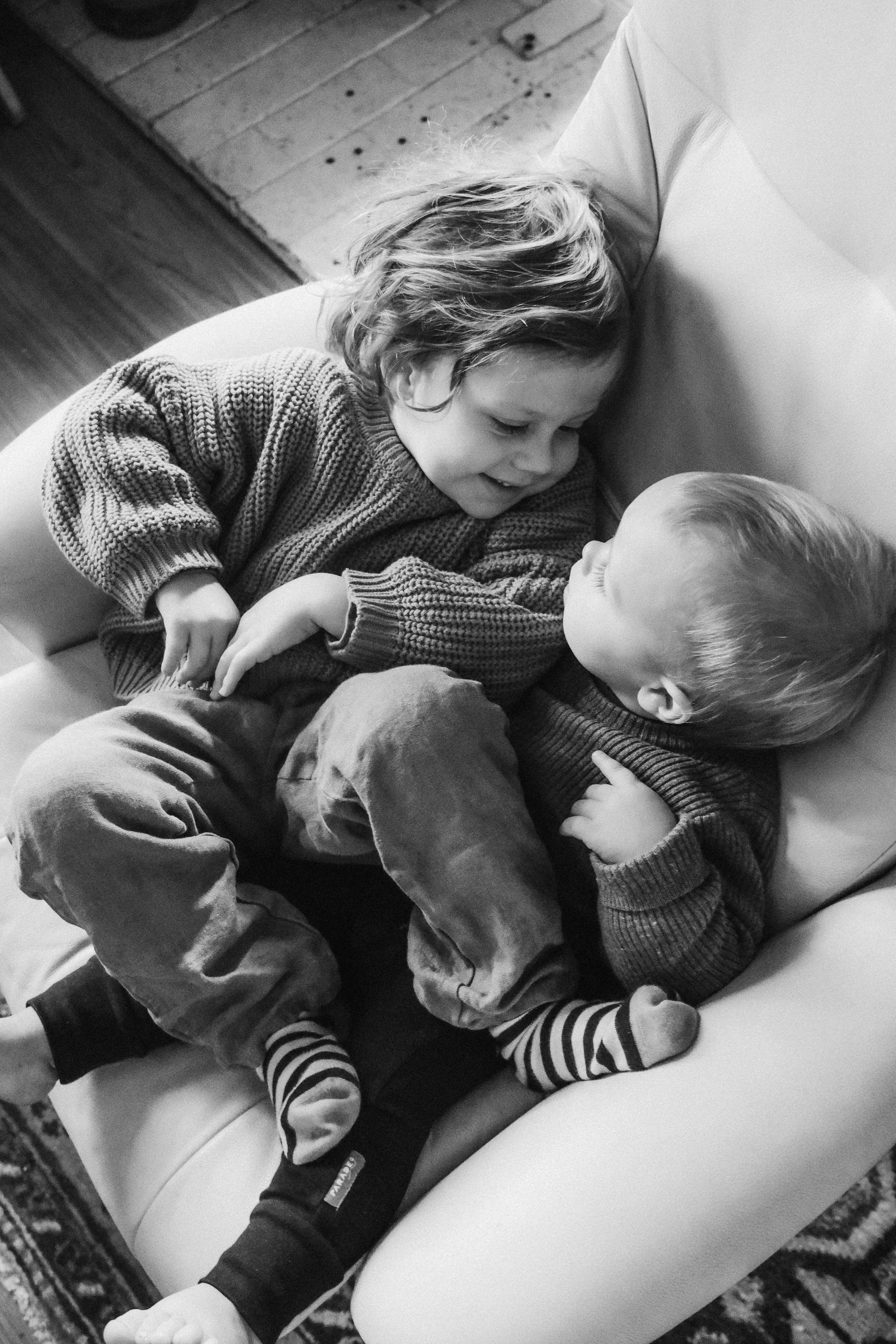 Two young children, a girl and a boy, lying on a couch, gazing at each other, smiling, in a cozy indoor setting.