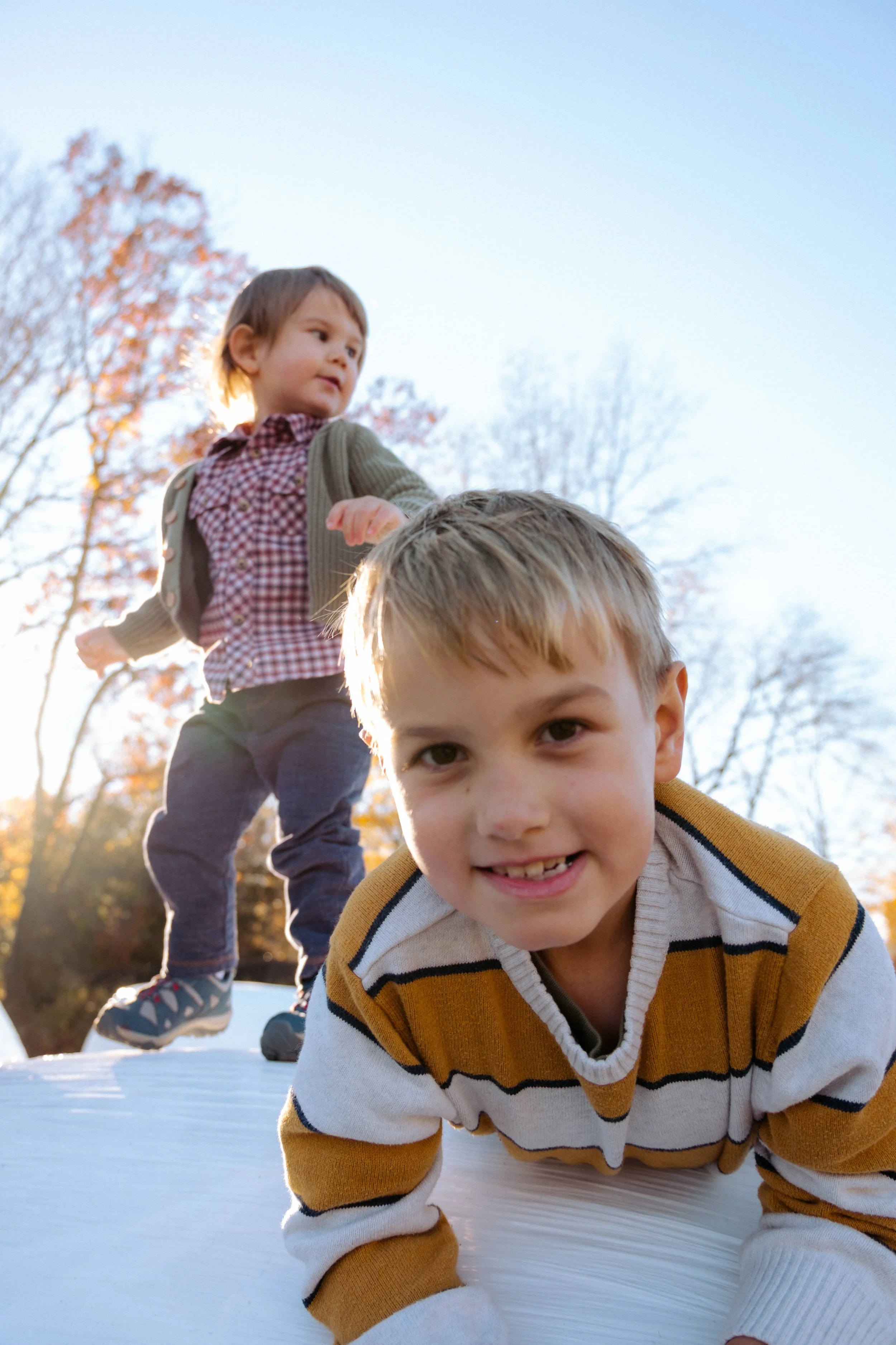 Two children playing outdoors on a sunny day, with trees in the background and an autumn setting.