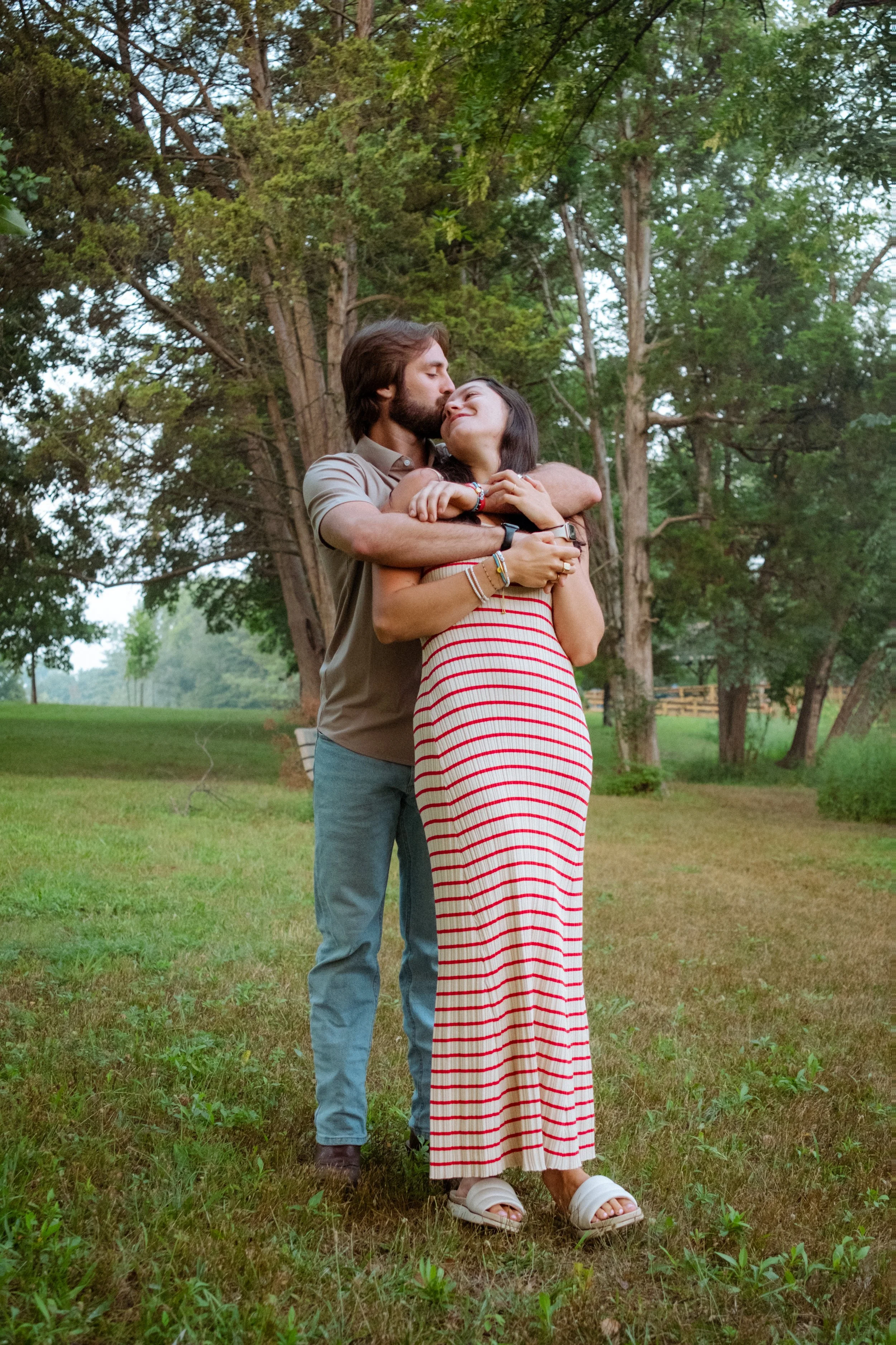 A couple embracing outdoors in a park with green trees and grass.