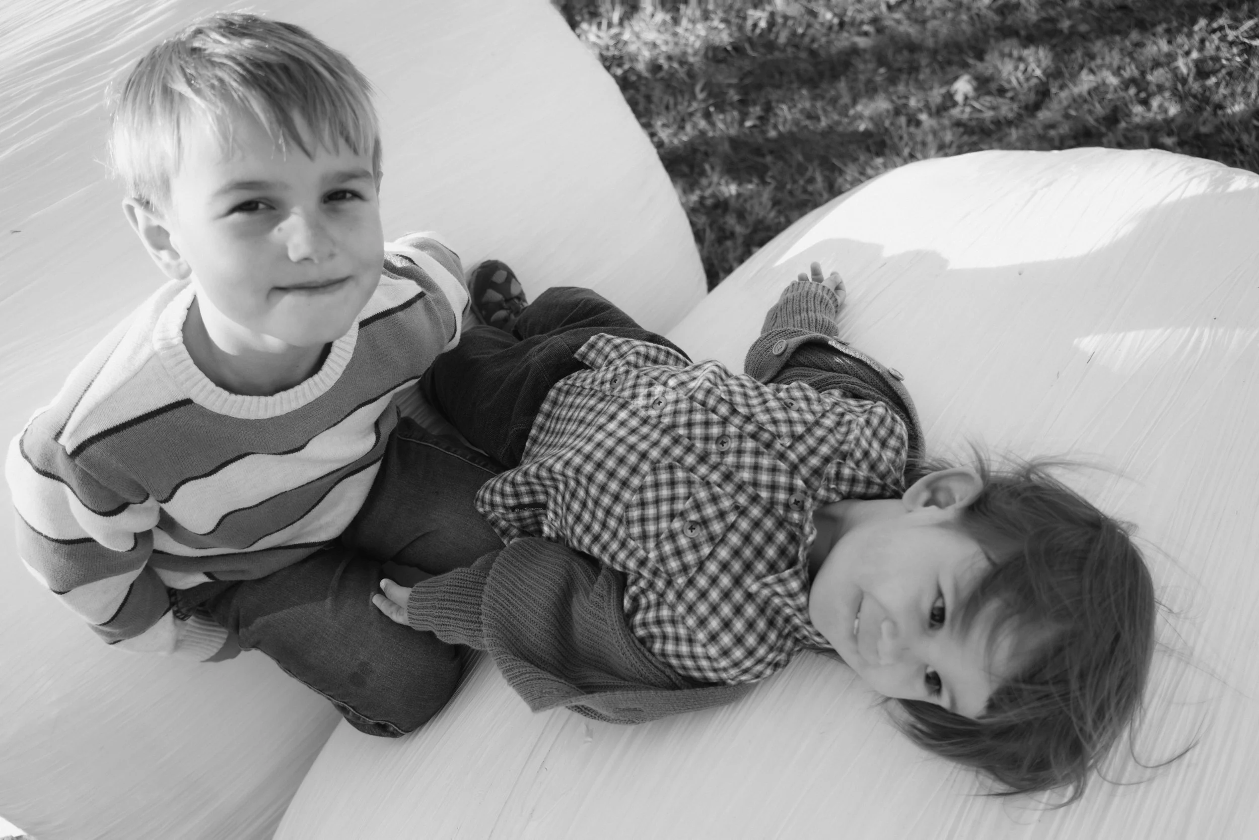 Two young children, a boy and a girl, on a playground structure, with the boy smiling at the camera and the girl lying down on the structure.