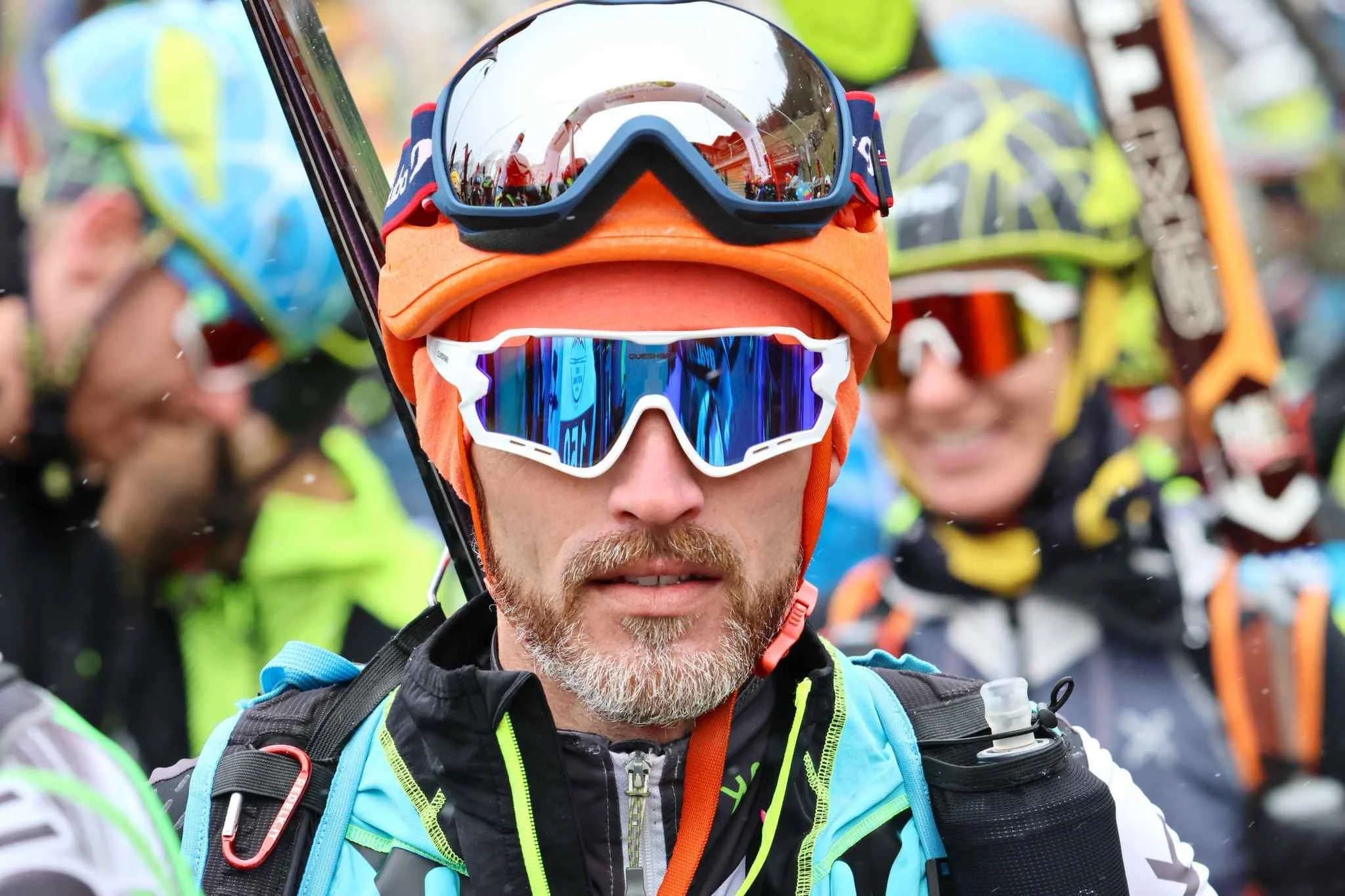 Ragazzo con capelli corti, camicia di jeans e maglietta a righe, che guarda verso sinistra con sfondo di edifici moderni.