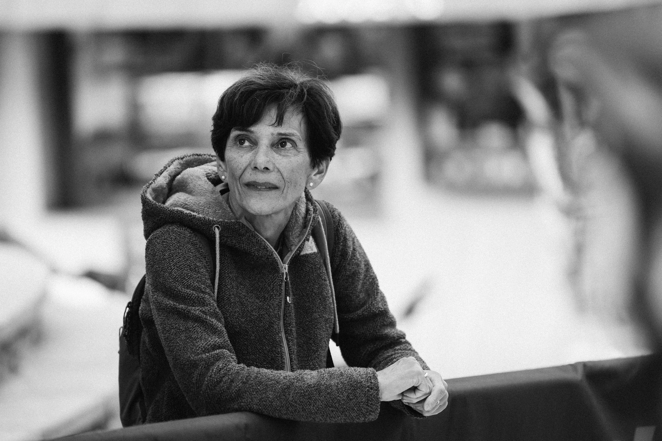 Ragazza con viso sorridente, indossa occhiali e giacca verde oliva, con sfondo di fogliame autunnale.