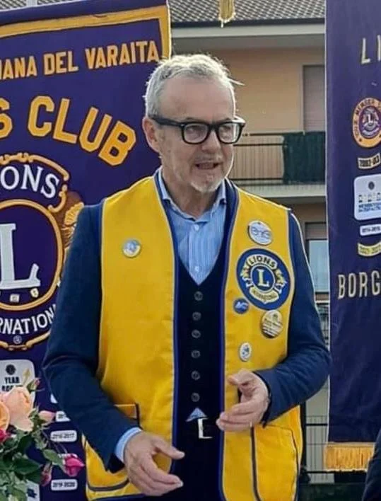 Uomo con barba, occhiali trasparenti e capelli ricci, che sorride leggermente.