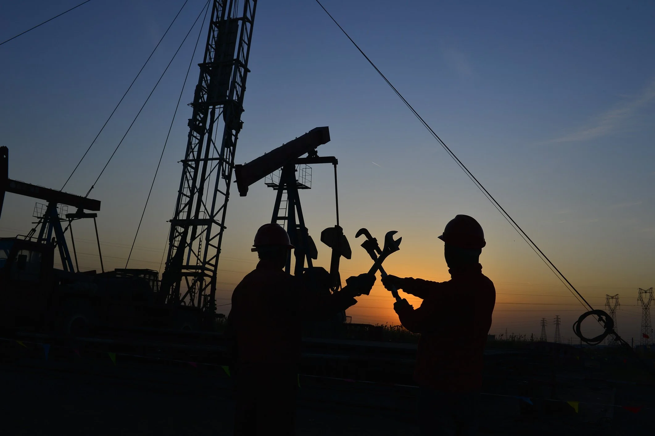Silhouettes of two workers in safety helmets exchanging tools at an oil rig during sunset.