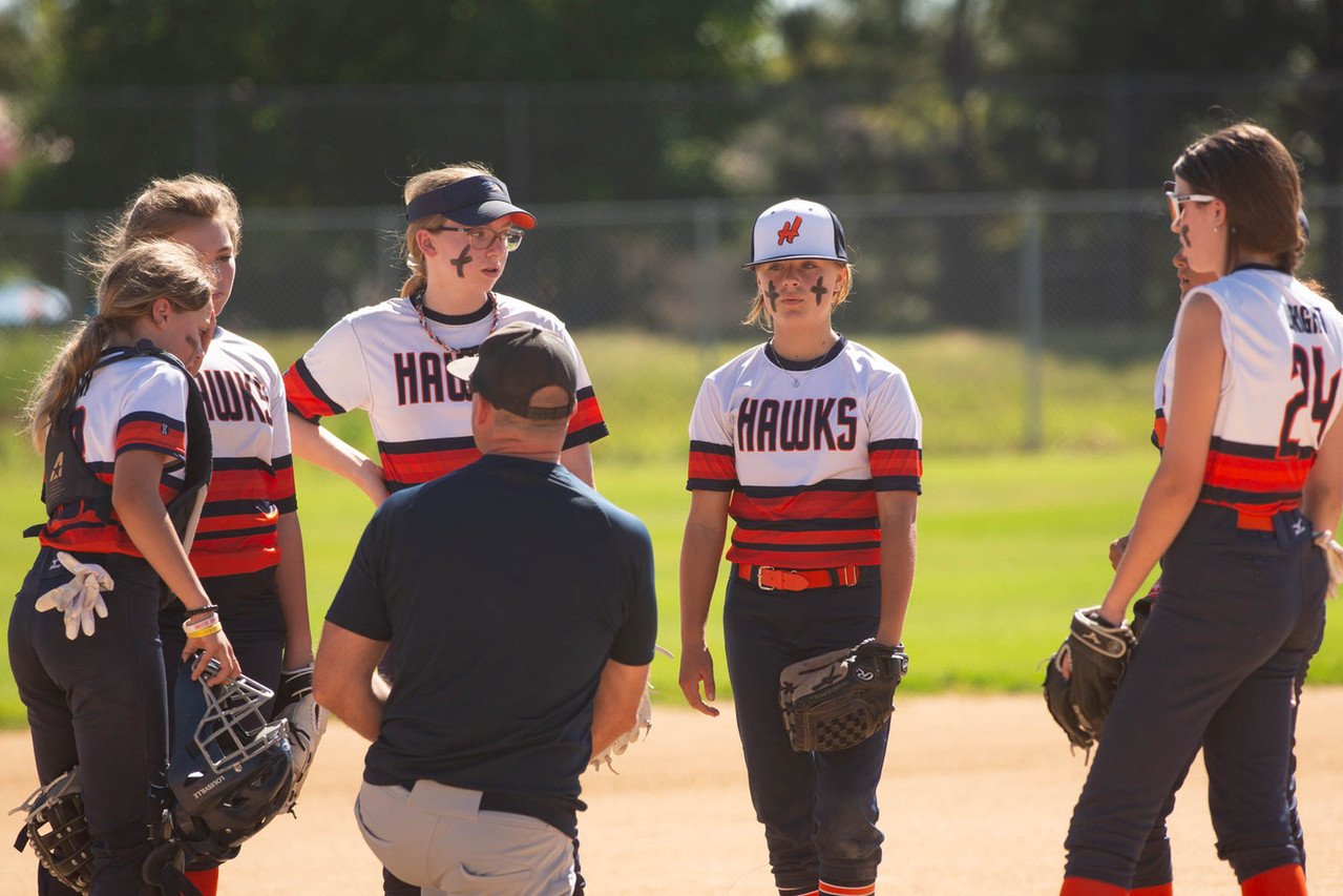 Girls' softball team called the Hawks listening to coach on a sunny field