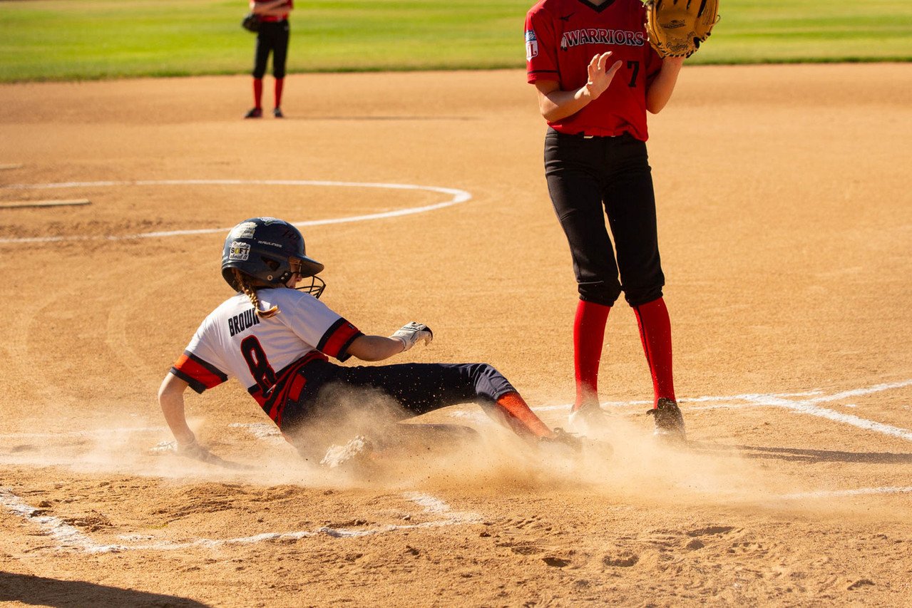 A female softball player sliding into a base as another player stands nearby on the field.