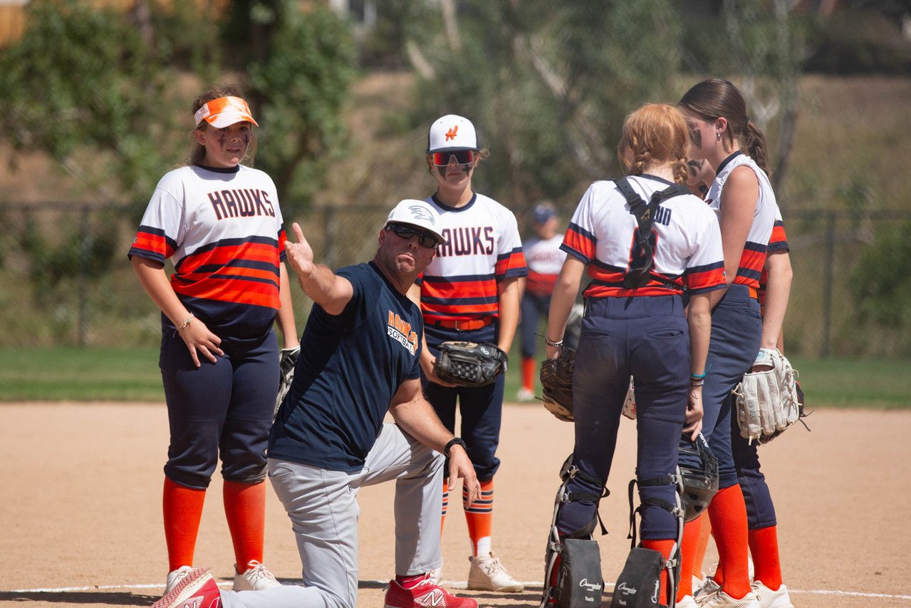 Softball coach giving instructions to team on field during game.