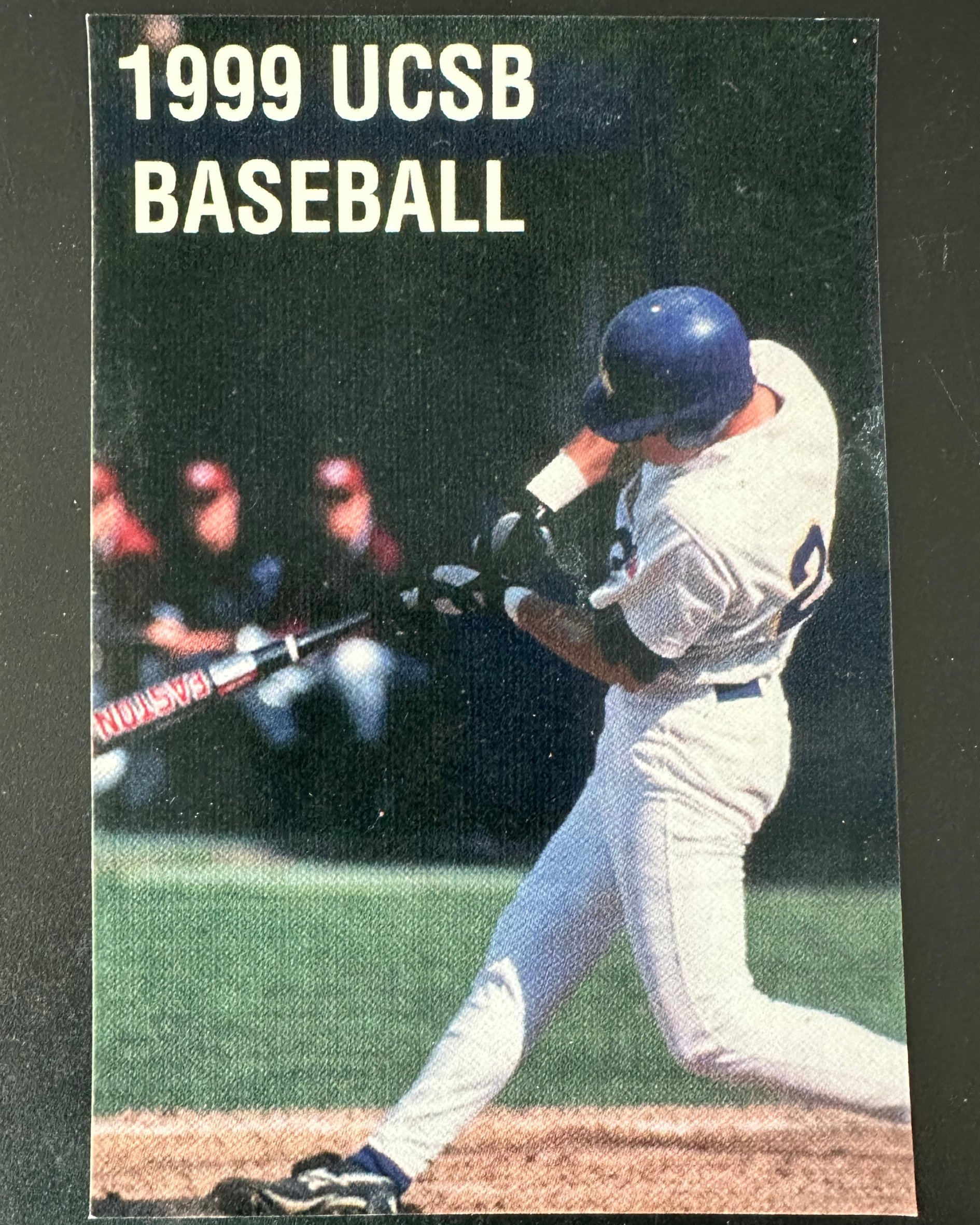 A baseball player in a uniform, wearing a helmet, batting during a game, with an audience in the background. The image is part of a 1999 UCSB Baseball publication or poster.
