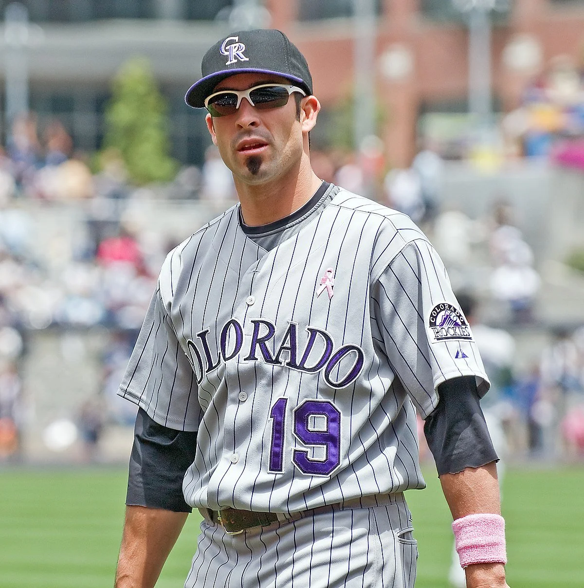 A baseball player in a Colorado Rockies uniform standing on the field, wearing sunglasses and a cap, during a game.