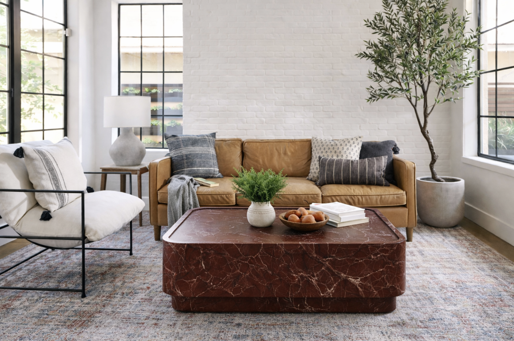 Living room with a brown leather sofa, white armchair, and large potted plant by window, with a red marble coffee table in front.
