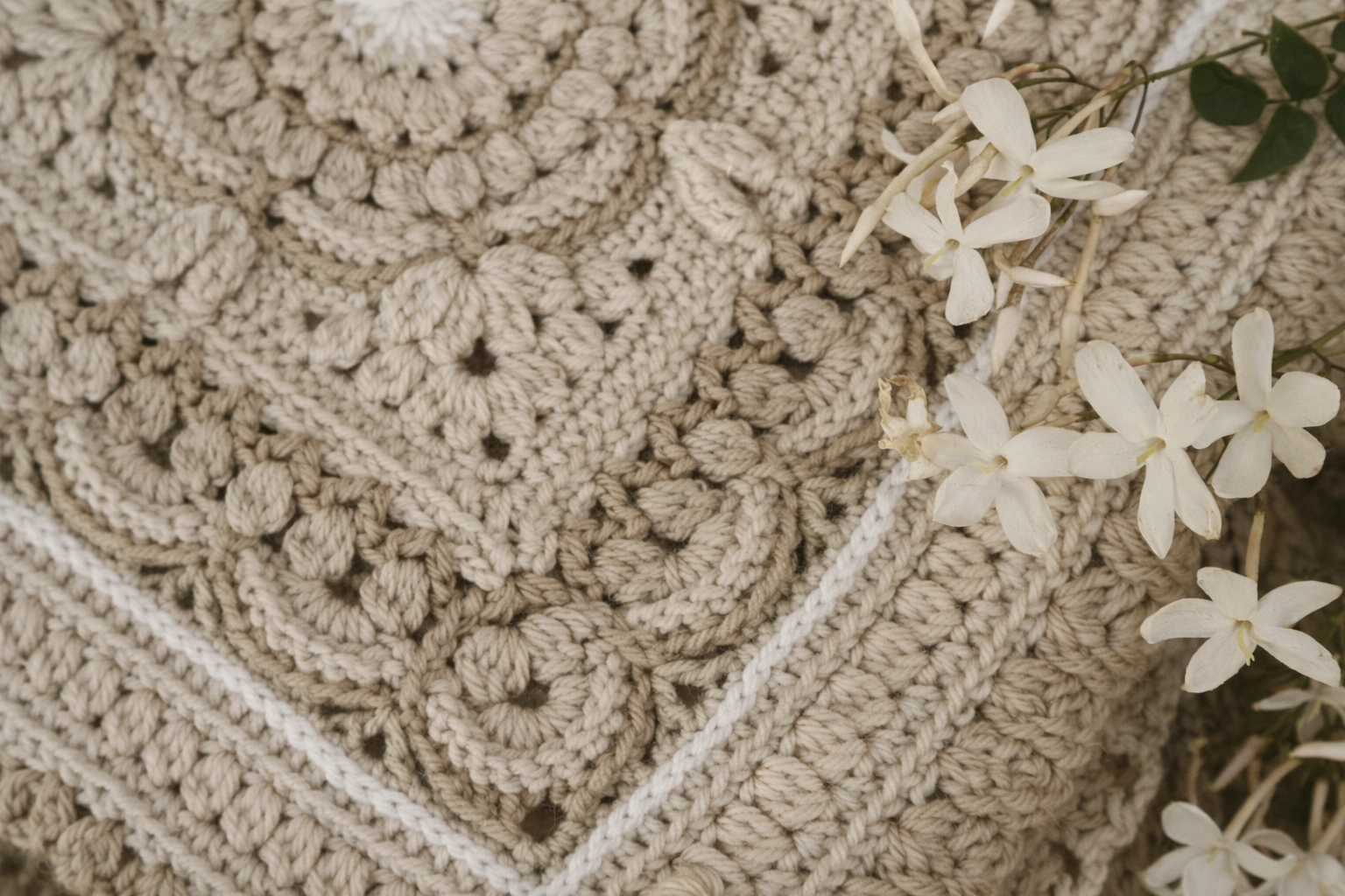 Close-up of a textured beige crochet blanket with white flowers resting on it.