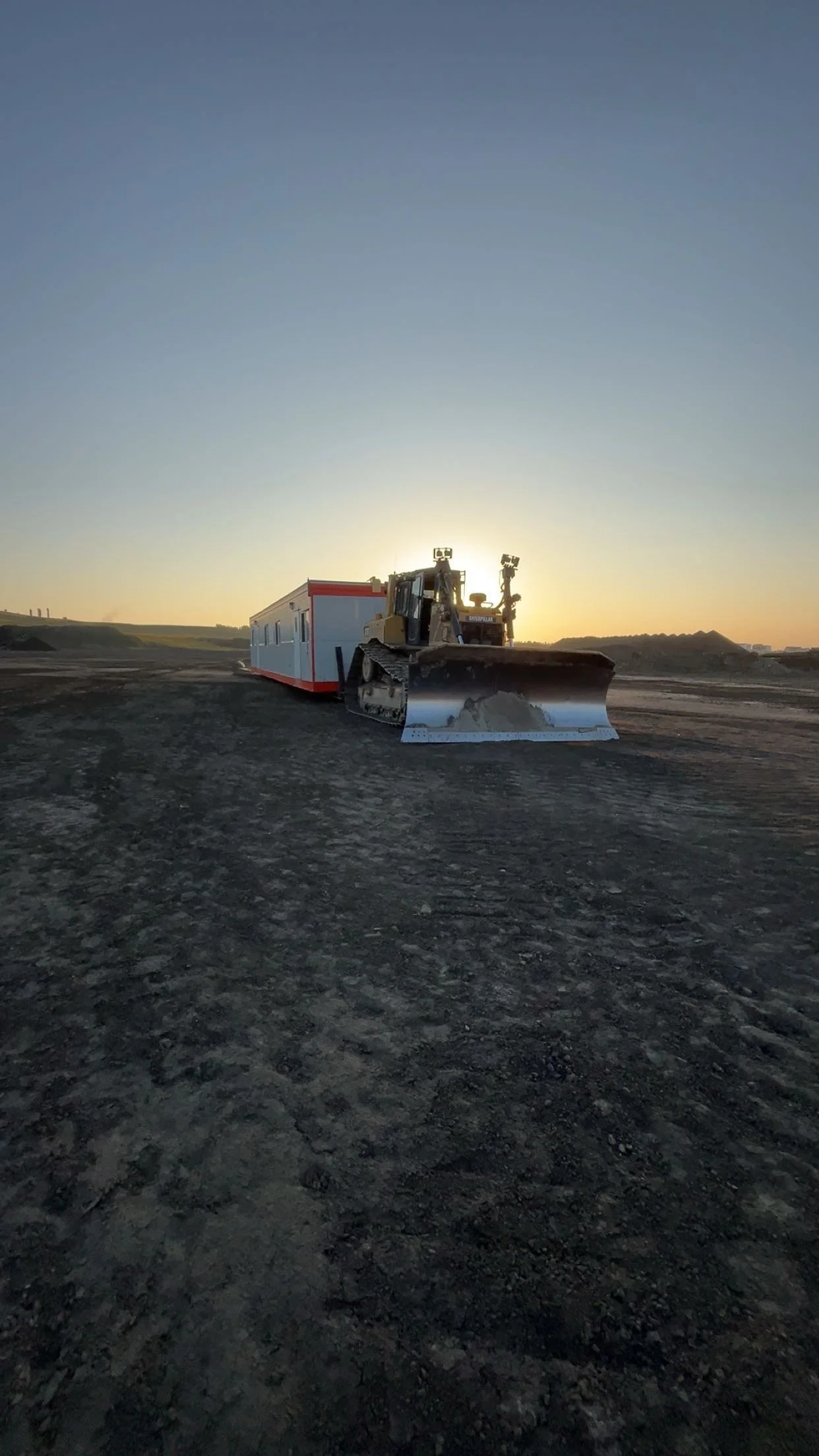 Construction site with a bulldozer and a mobile office trailer during sunset.