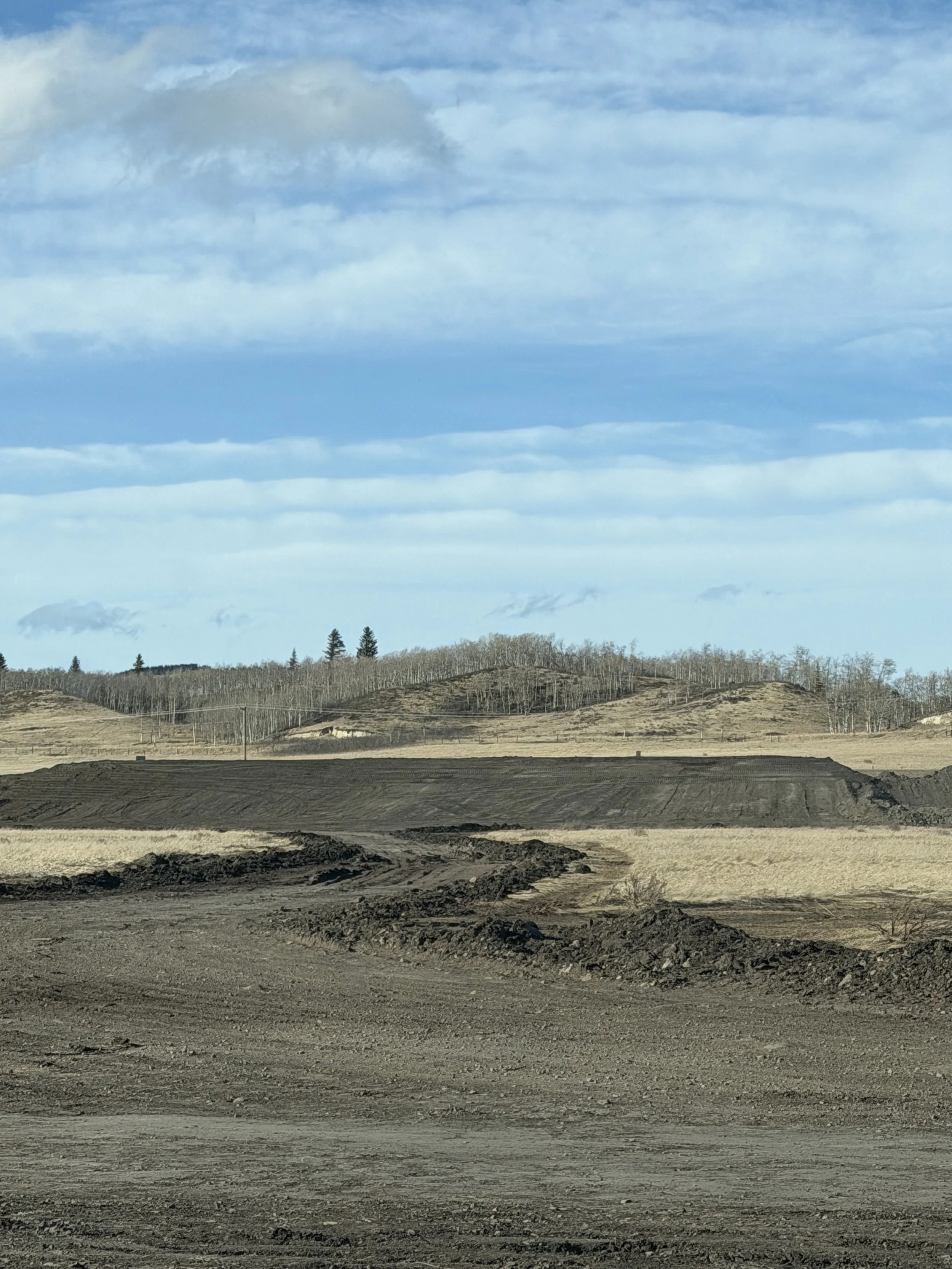 A landscape with dry soil in the foreground, sawtooth hills in the middle, and a blue sky with clouds above.