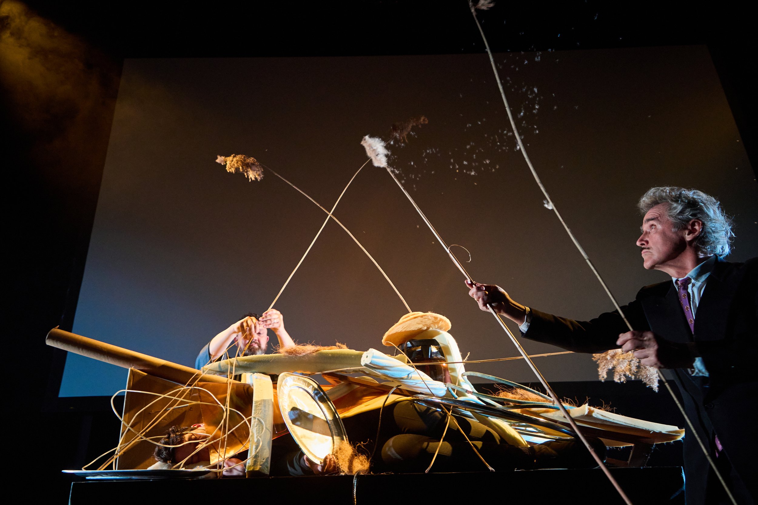 Scene from Ikebana B.K.S. Yesterday and Today by František Skála, performed during the opening of the GA-I-SU-RA exhibition, with two performers constructing a large abstract ikebana-like sculpture over a human figure in a dark theatrical space.