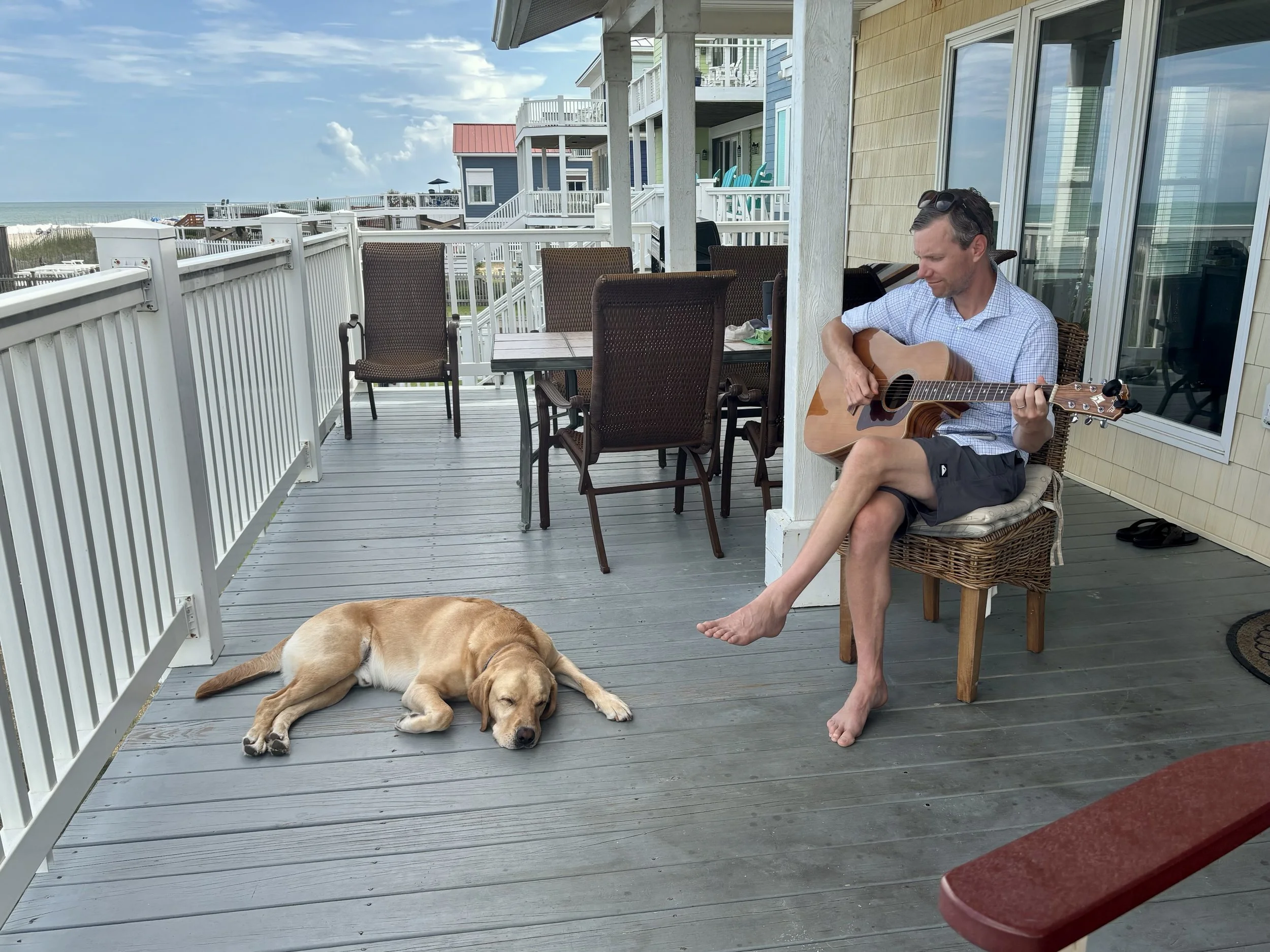 Rich Doyle playing guitar on a porch with Buddy resting nearby.