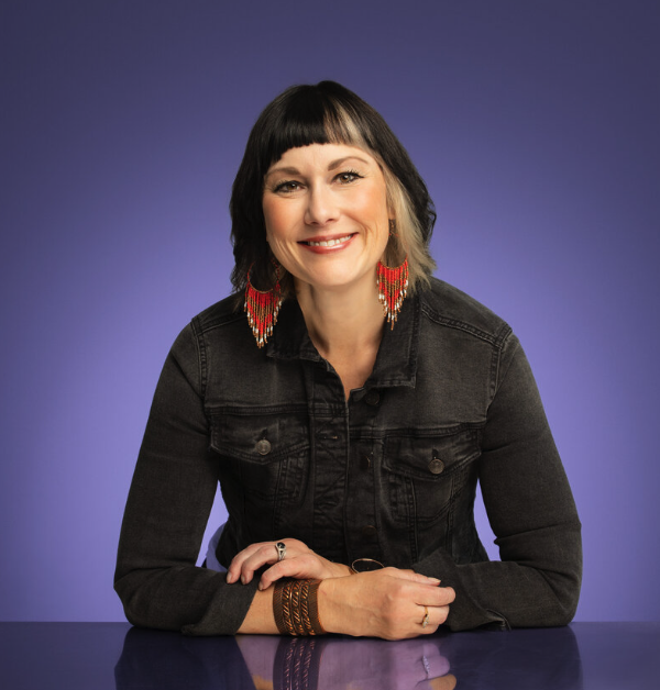 Woman with short brown hair smiling, wearing hoop earrings and a necklace, against a blue and yellow background with a certification badge reading 'StoryBrand Certified Guide'.