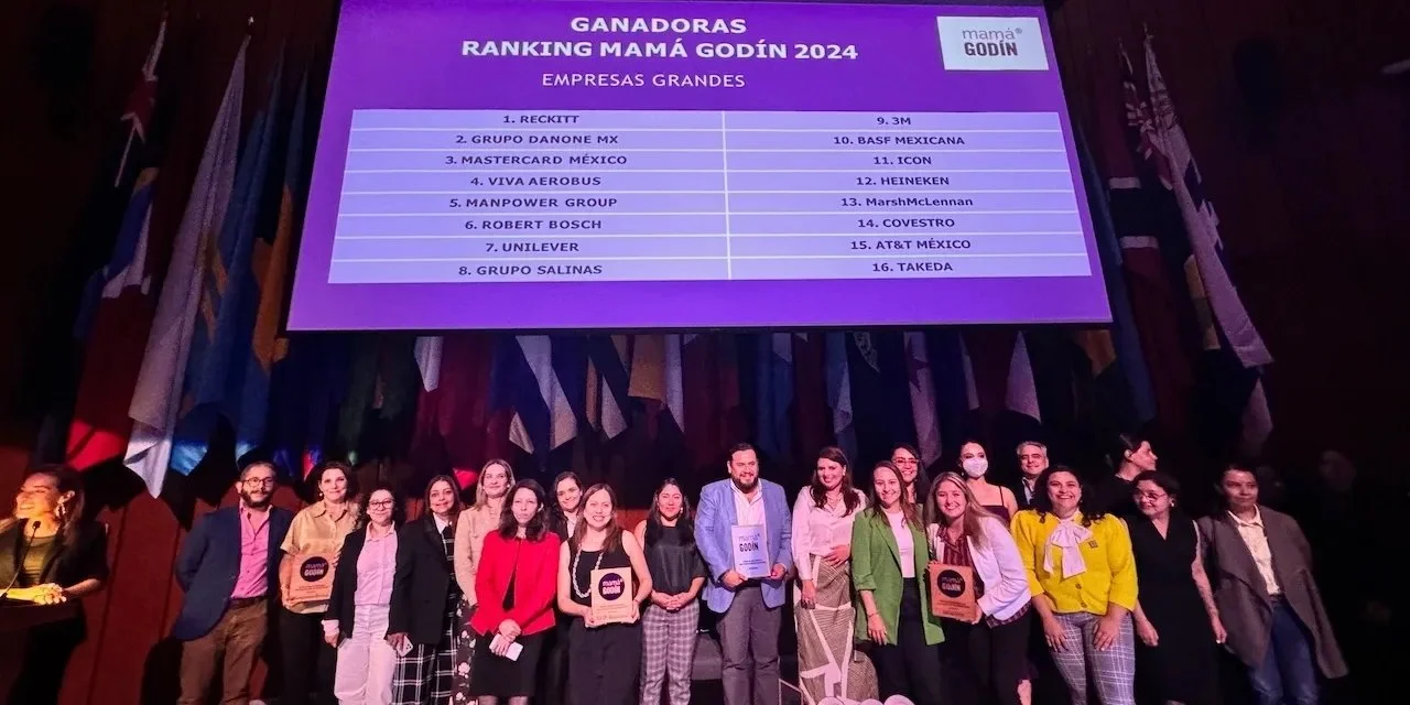 Foto de un grupo de personas en un escenario, con un gran cartel que muestra la lista de ganadoras del ranking Mamá Godín 2024 en empresas grandes, en un evento formal.