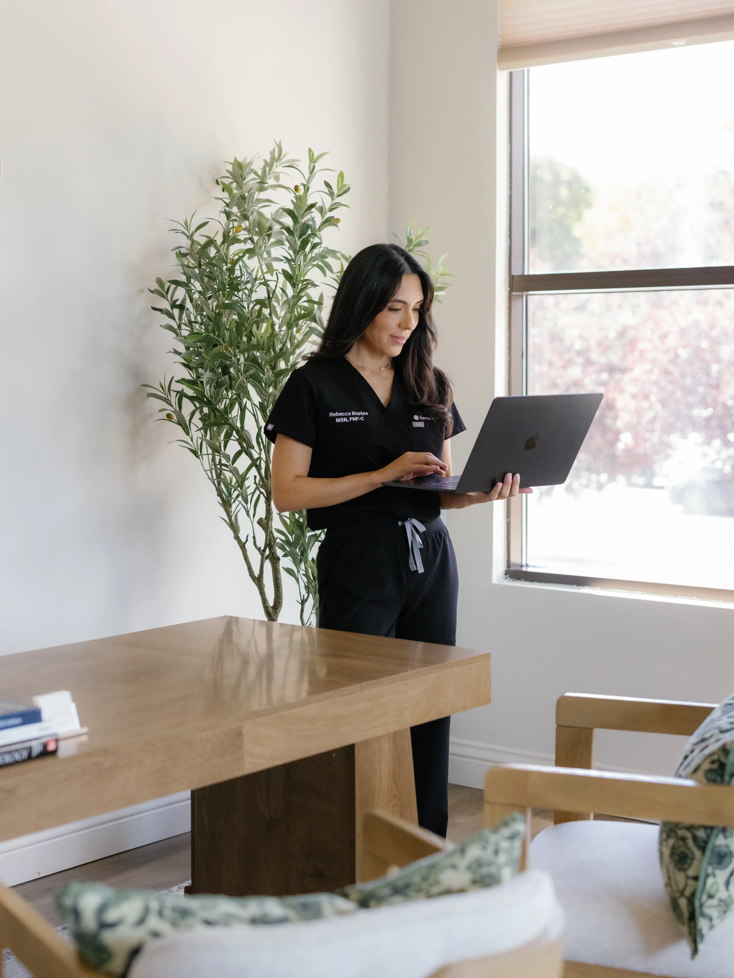 Nurse practitioner in scrubs looking at work laptop