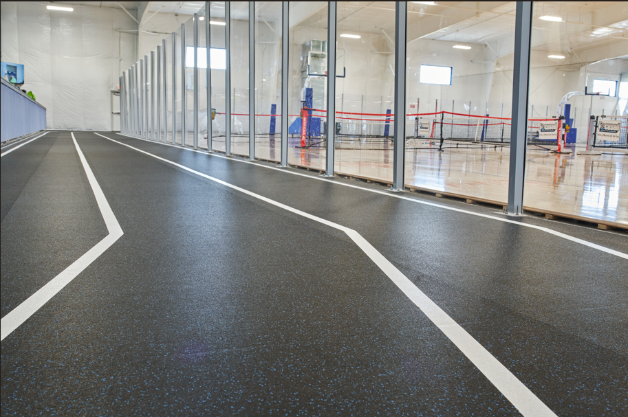 Indoor running track next to an enclosed sports court with a wooden floor and net for sports like volleyball or tennis.