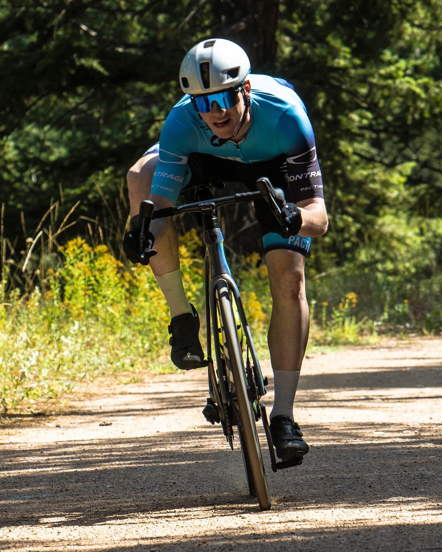 Cyclist wearing a white helmet, blue jersey, and black shorts rides a mountain bike on a dirt trail through a forest. private mens style consultant boulder Colorado personal styling styled by swift. sonic boom racing team cycling