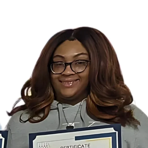 Woman with wavy brown hair, wearing glasses and a grey hoodie, smiling and holding a certificate.