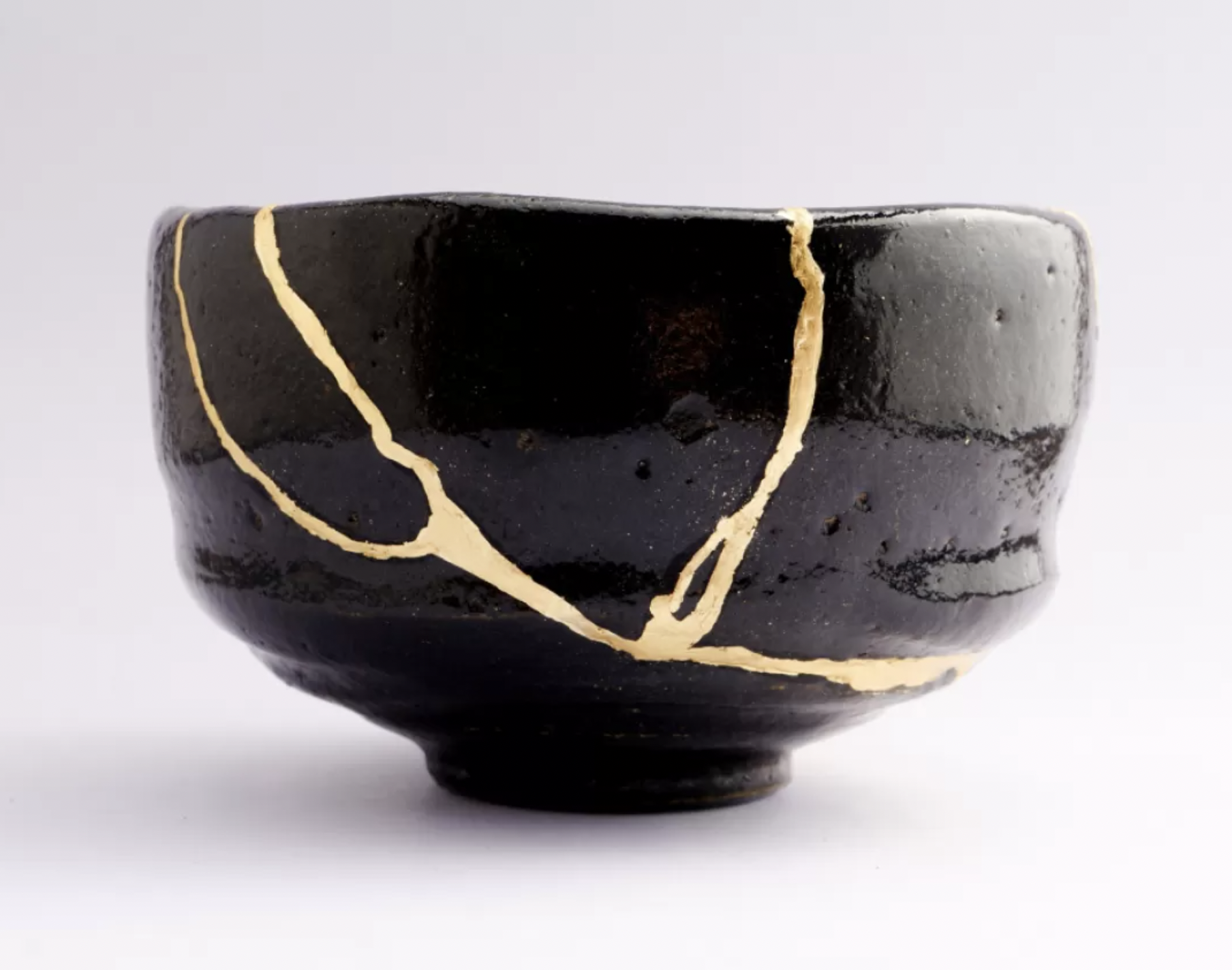 Close-up image of a black ceramic cup with gold-colored crackle glaze on a white background.