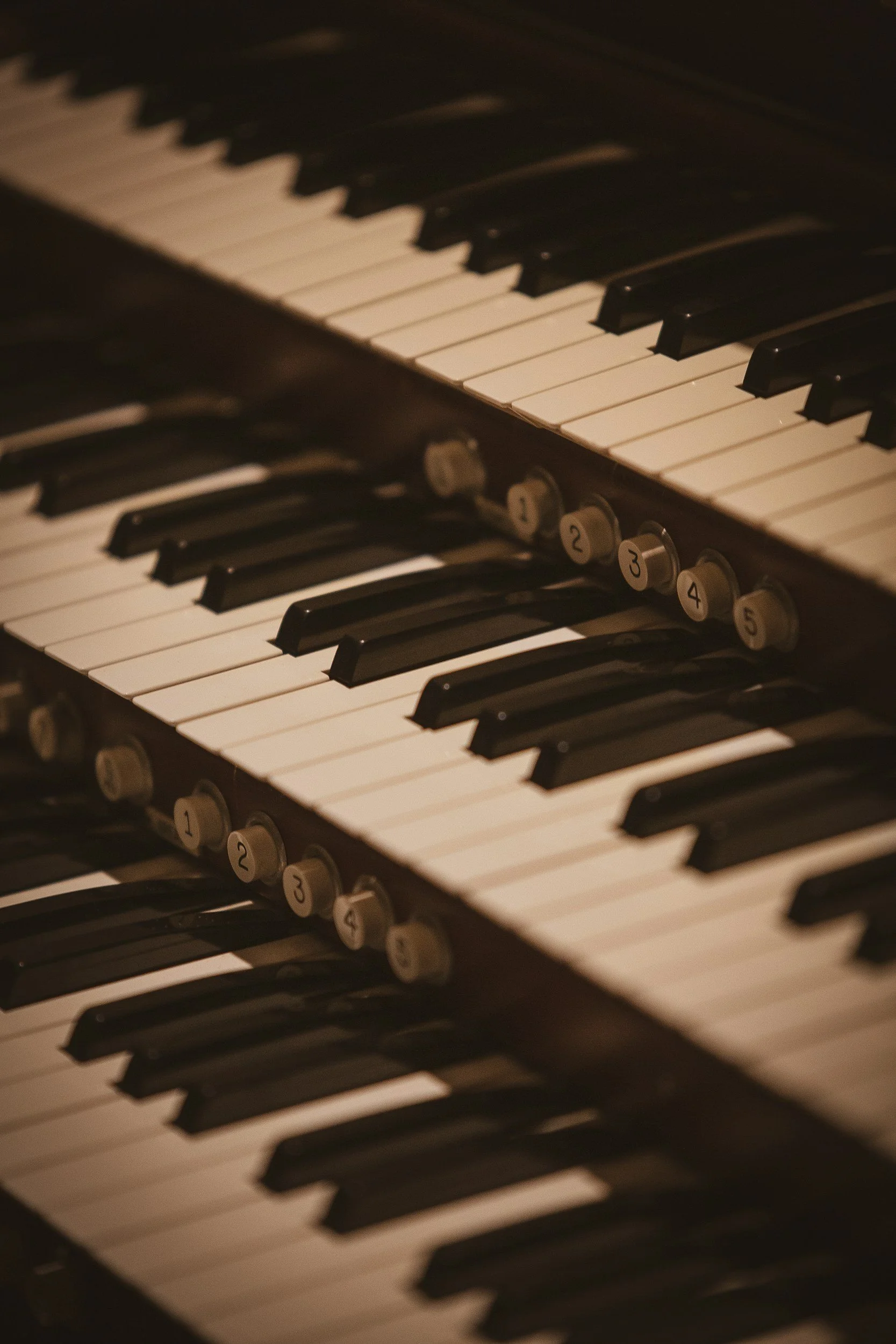 Close-up of a vintage organ keyboard showing black and white keys and rotary switches numbered 1 to 5.