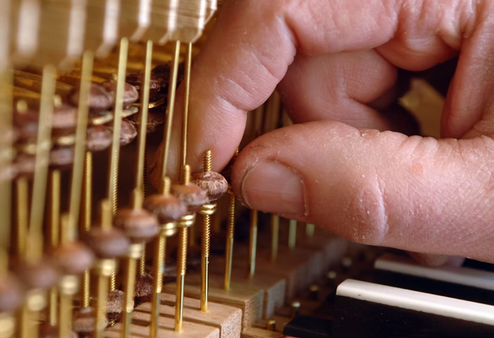 Close-up of a person's hand adjusting the tuning pins inside a piano.