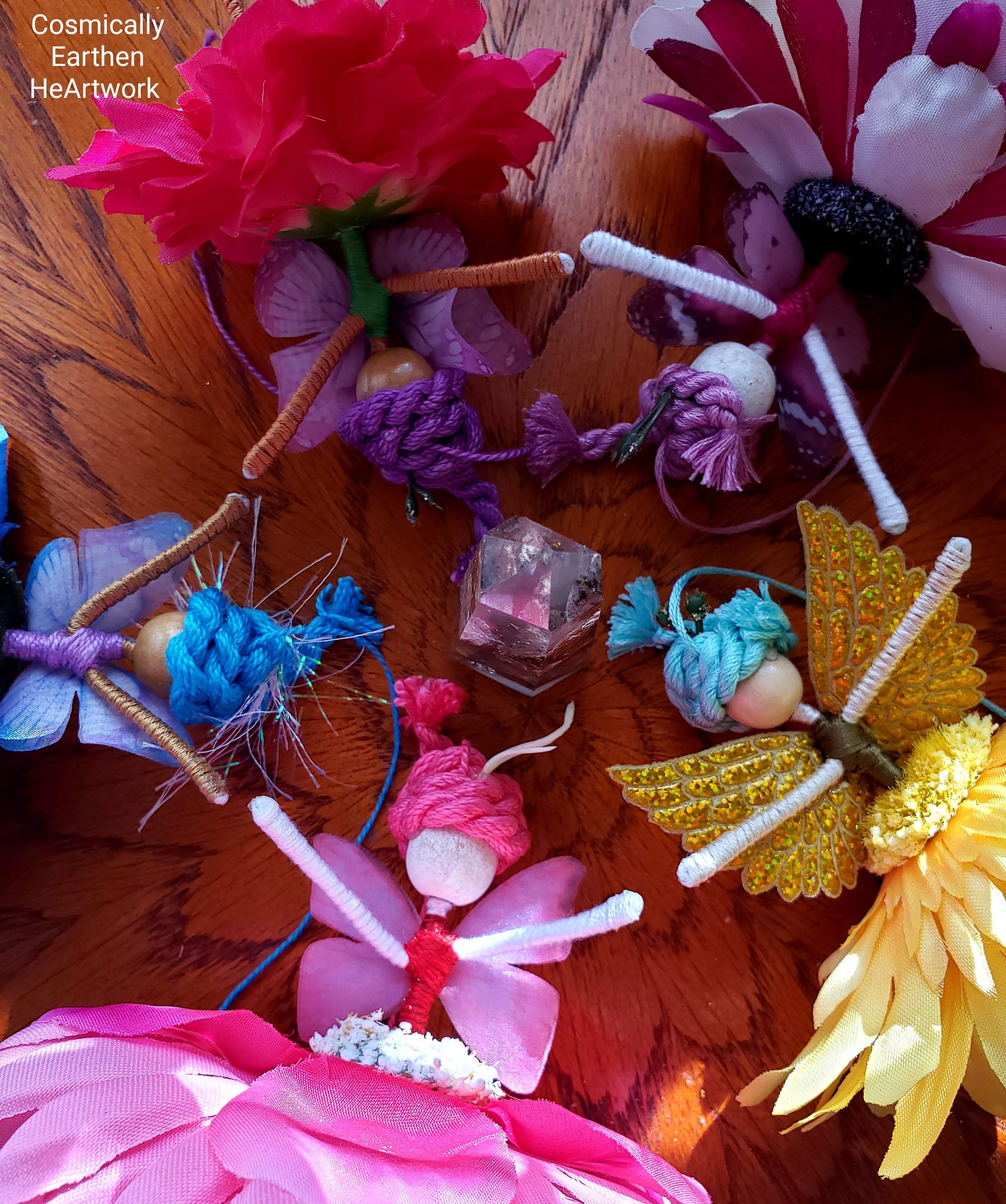 Colorful handcrafted fairy and butterfly decorations with flowers, beads, and a crystal on a wooden surface.