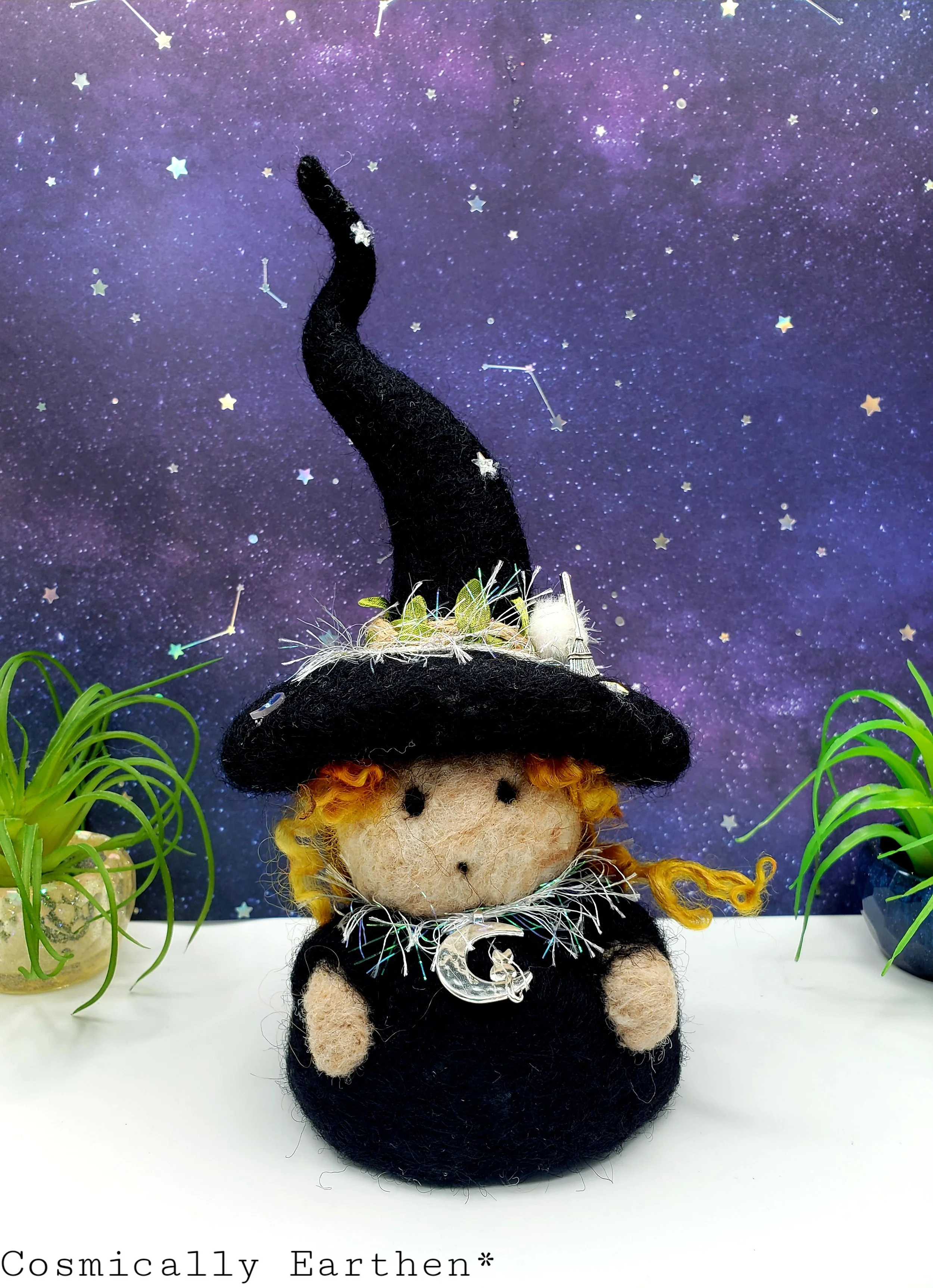Needle-felted Groundling trio with blue, black, and green hats, adorned with flowers, crystals, and charms, set against a starry background with small green plants.